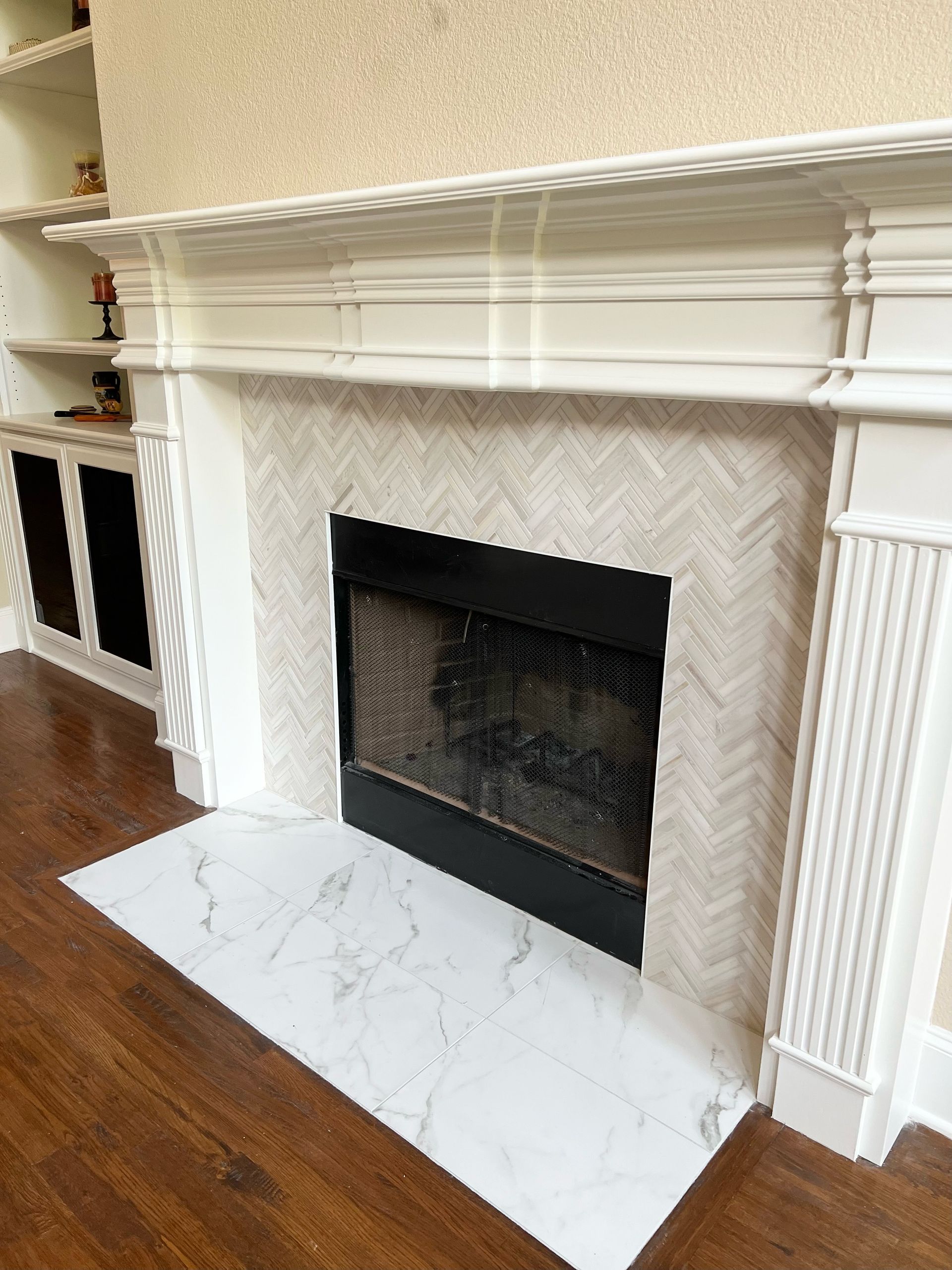 White marble fireplace with ornate mantel in a room with wood floors and built-in shelving