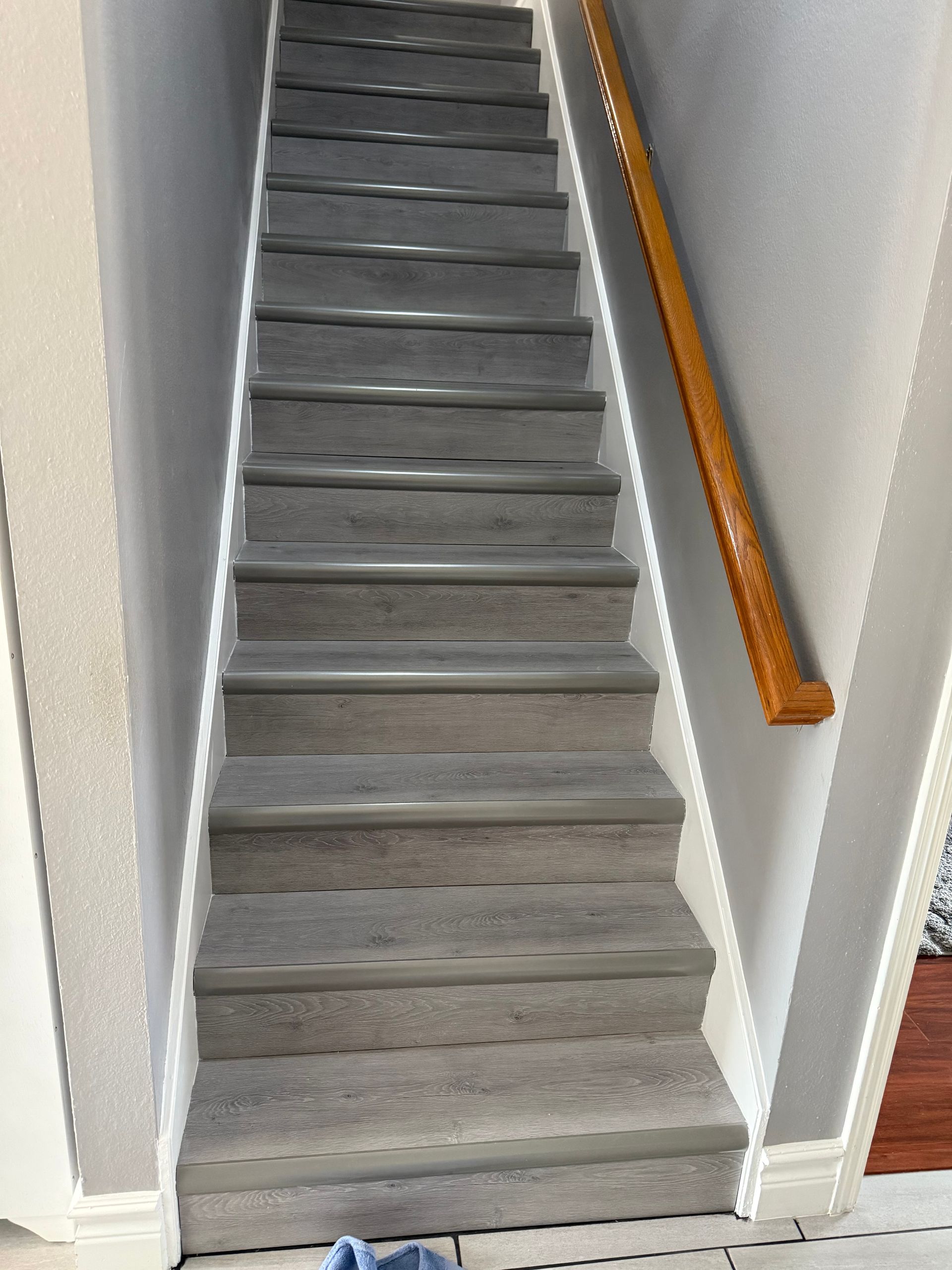 Narrow carpeted staircase with white walls and a wooden handrail on the right