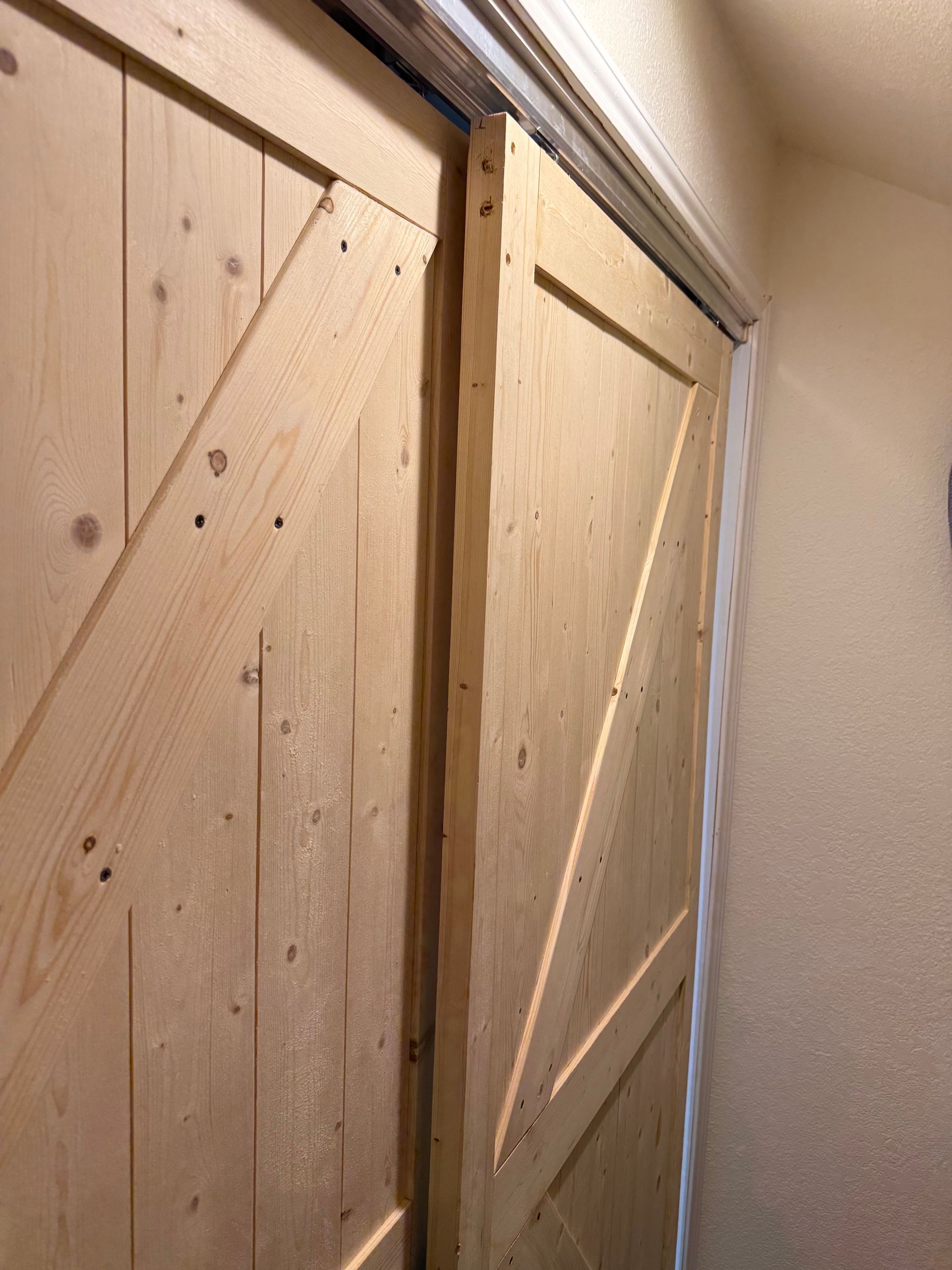 Close-up of a light wood sliding barn door with diagonal braces in a hallway