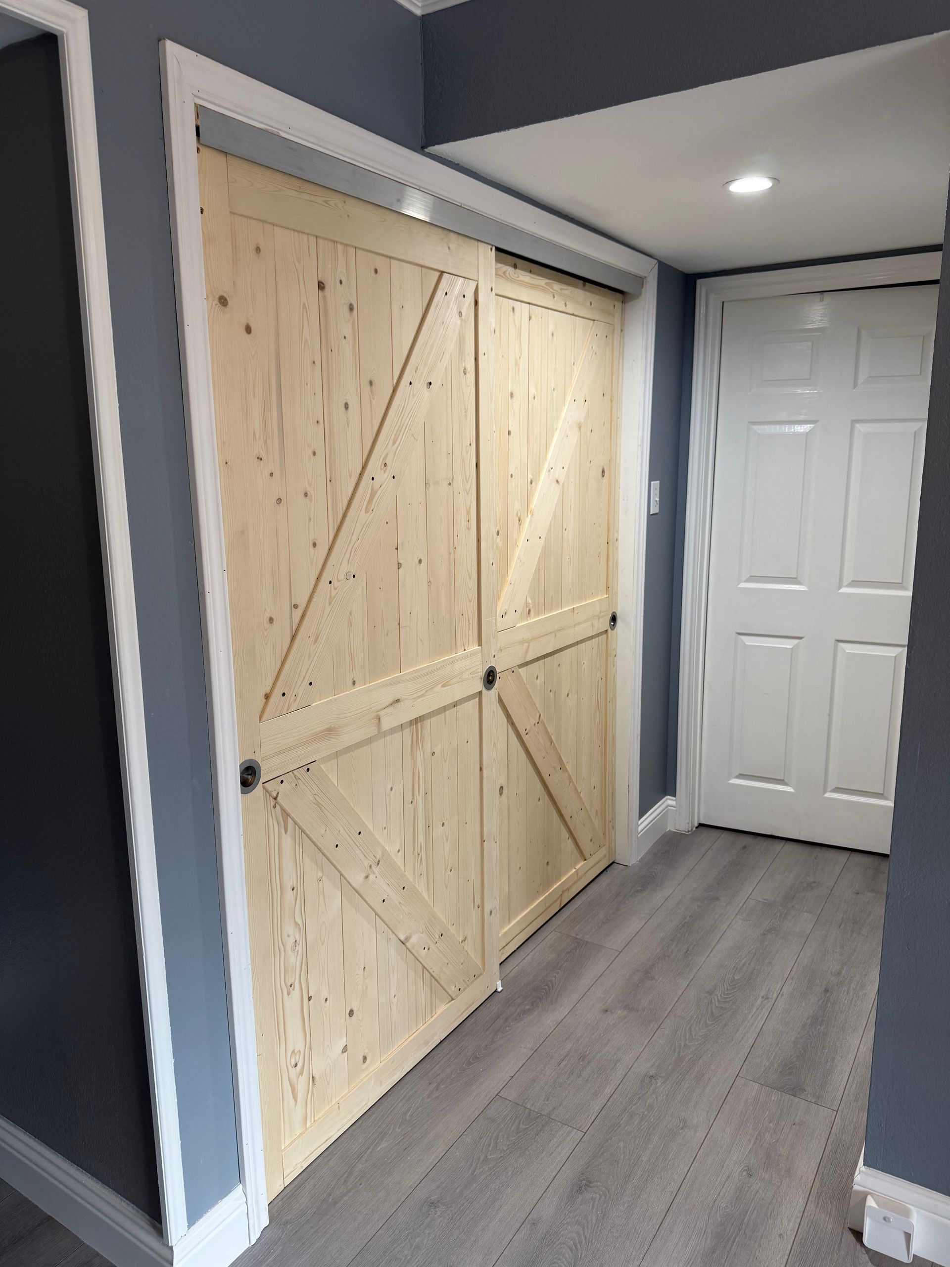 Hallway with large sliding barn doors made of unfinished wood and a white closet door on the right.
