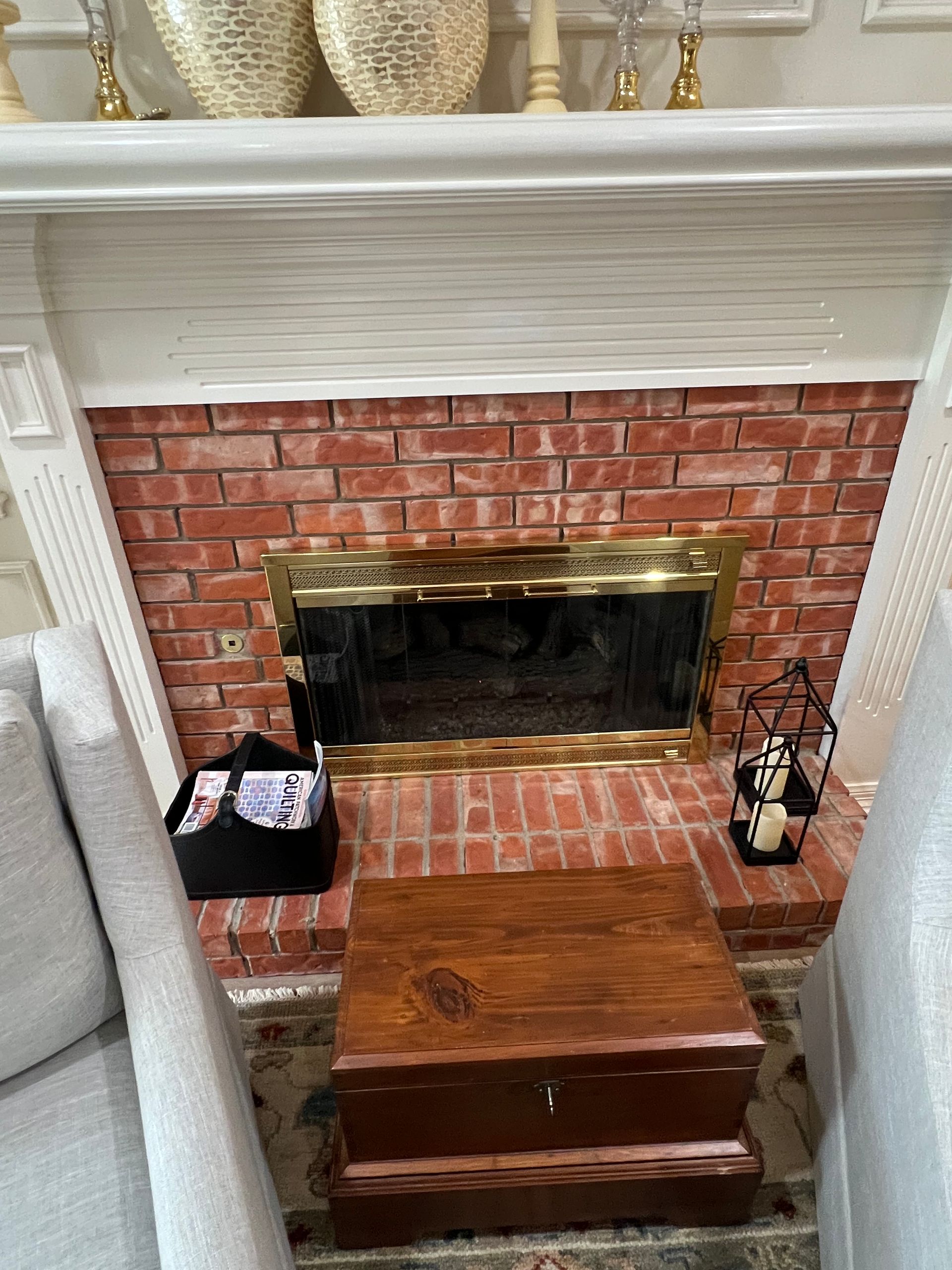 Brick fireplace with brass screen, wooden chest, and small decor in a living room