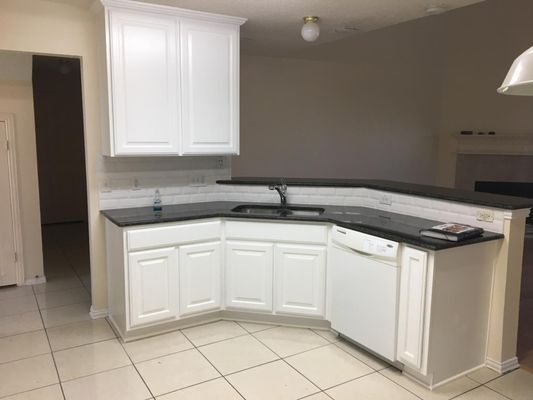 A kitchen with white cabinets , black counter tops , and a dishwasher.