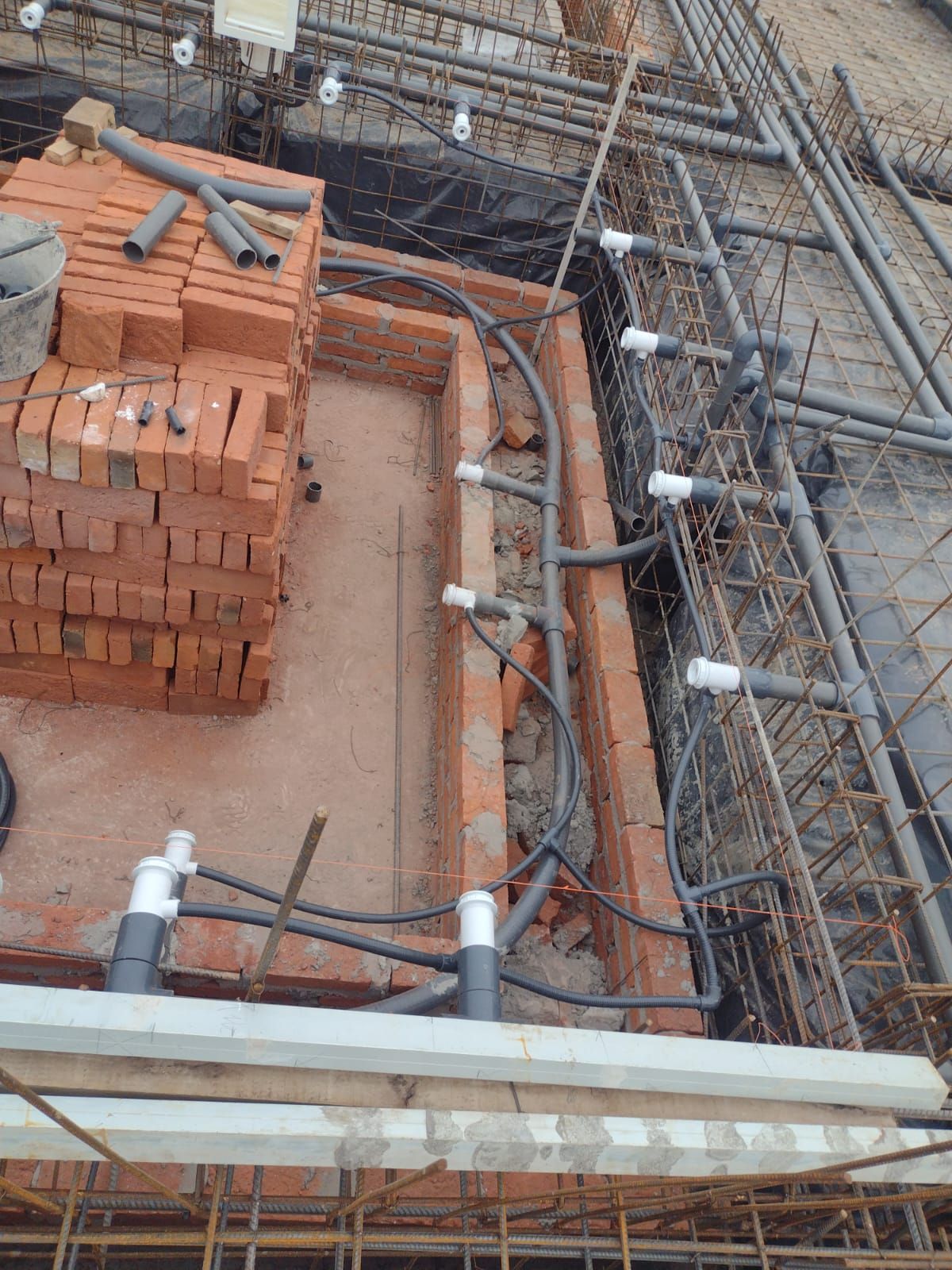 Obra en construcción: mampostería, tuberías y barras de refuerzo para el sistema de plomería en un área abierta.