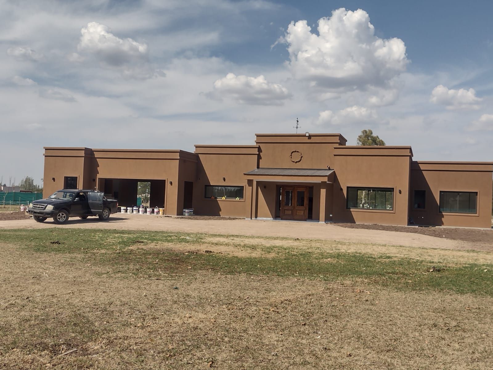 Edificio marrón con techo plano, bajo un cielo nublado. Un camión negro está estacionado enfrente.