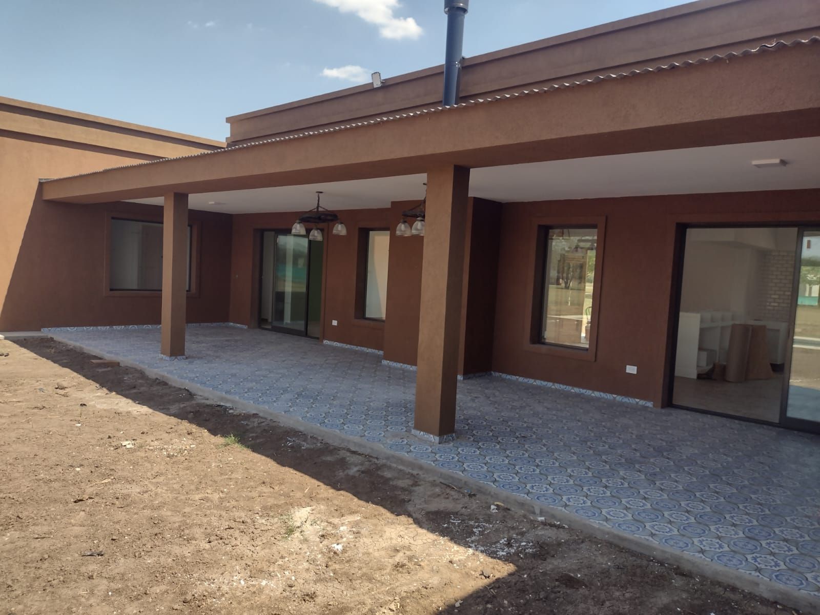 Exterior de la casa pintado de marrón con patio cubierto, suelo de grava y puertas correderas de cristal.