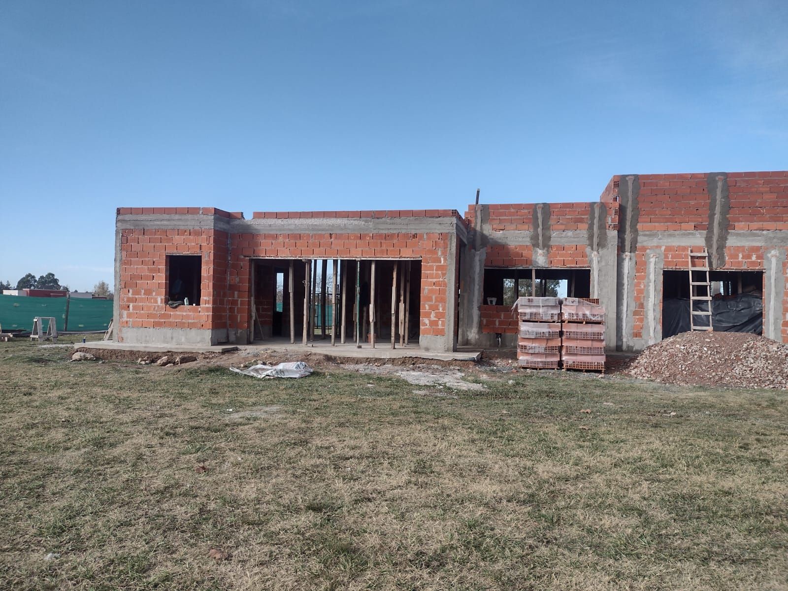Casa en construcción, paredes de ladrillo rojo, cielo azul, exterior.