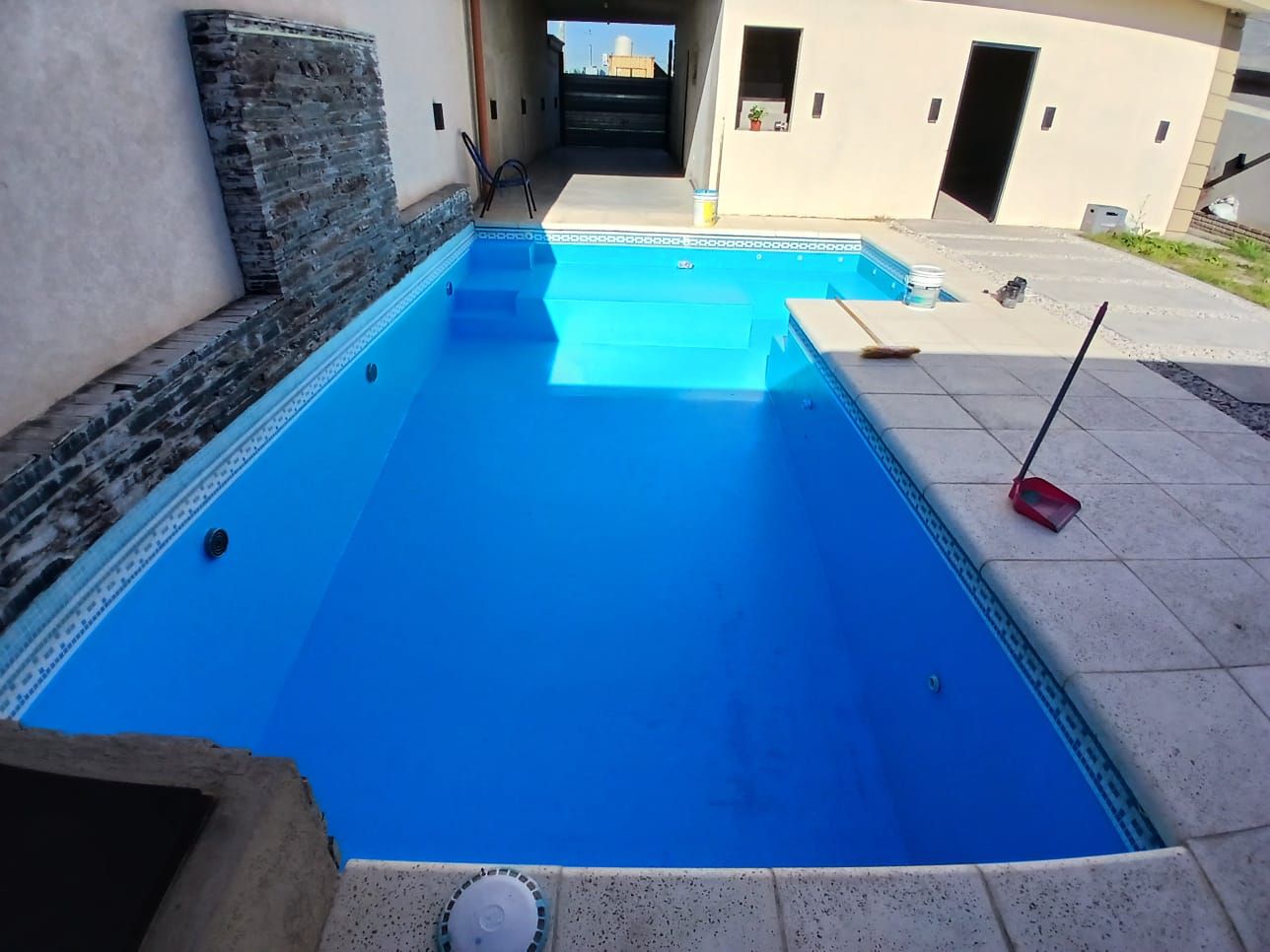 Una piscina rectangular llena de agua azul, rodeada por un patio y un edificio de piedra.
