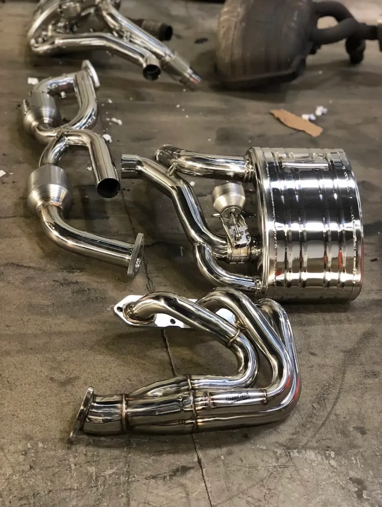 Shiny chrome car exhaust system components arranged on a concrete floor | Eastside Motoring