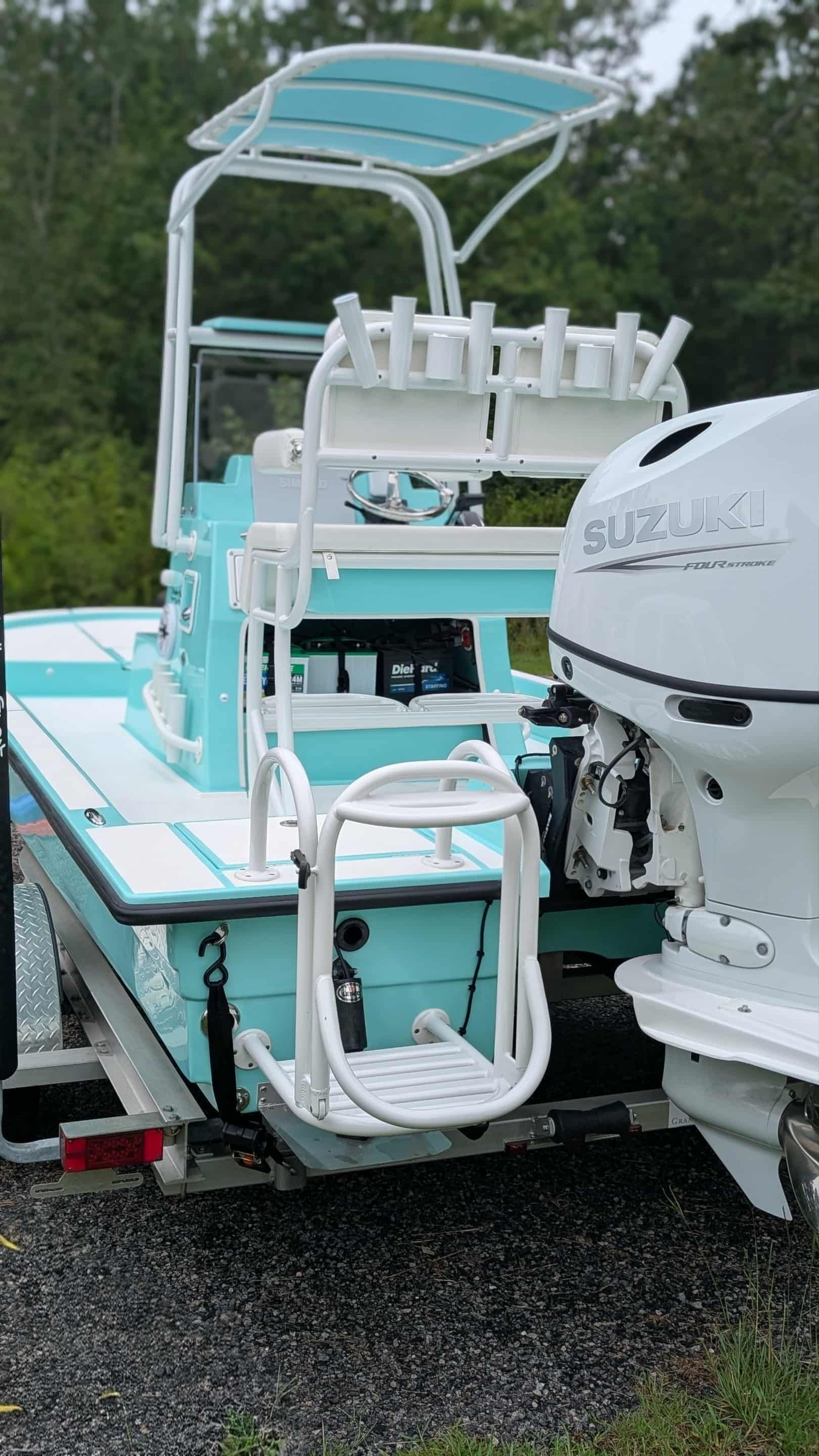 Rear view of a light blue and white fishing boat with a Suzuki outboard motor, parked on a trailer.
