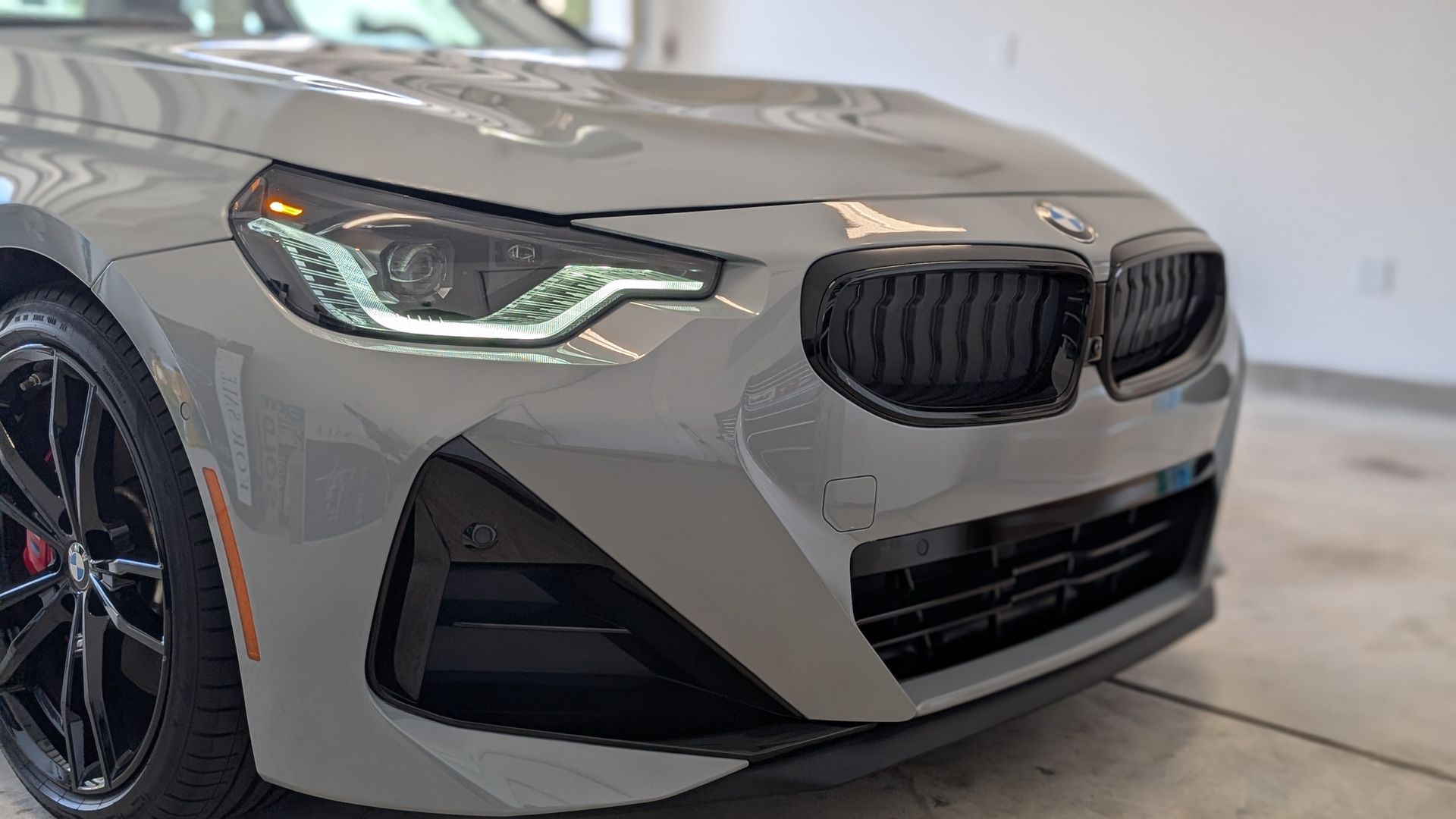 Gray BMW car's front with black grille, headlights, and a wheel.