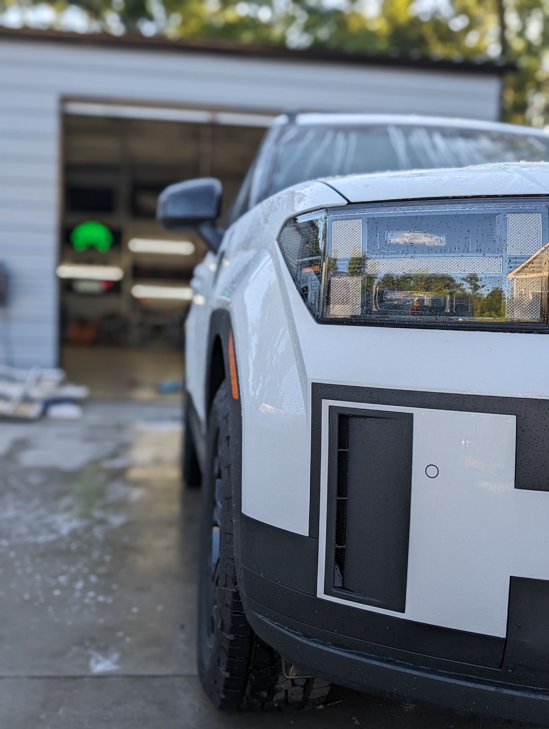 White electric SUV parked outside a garage. Close-up of front showing headlight and tire.