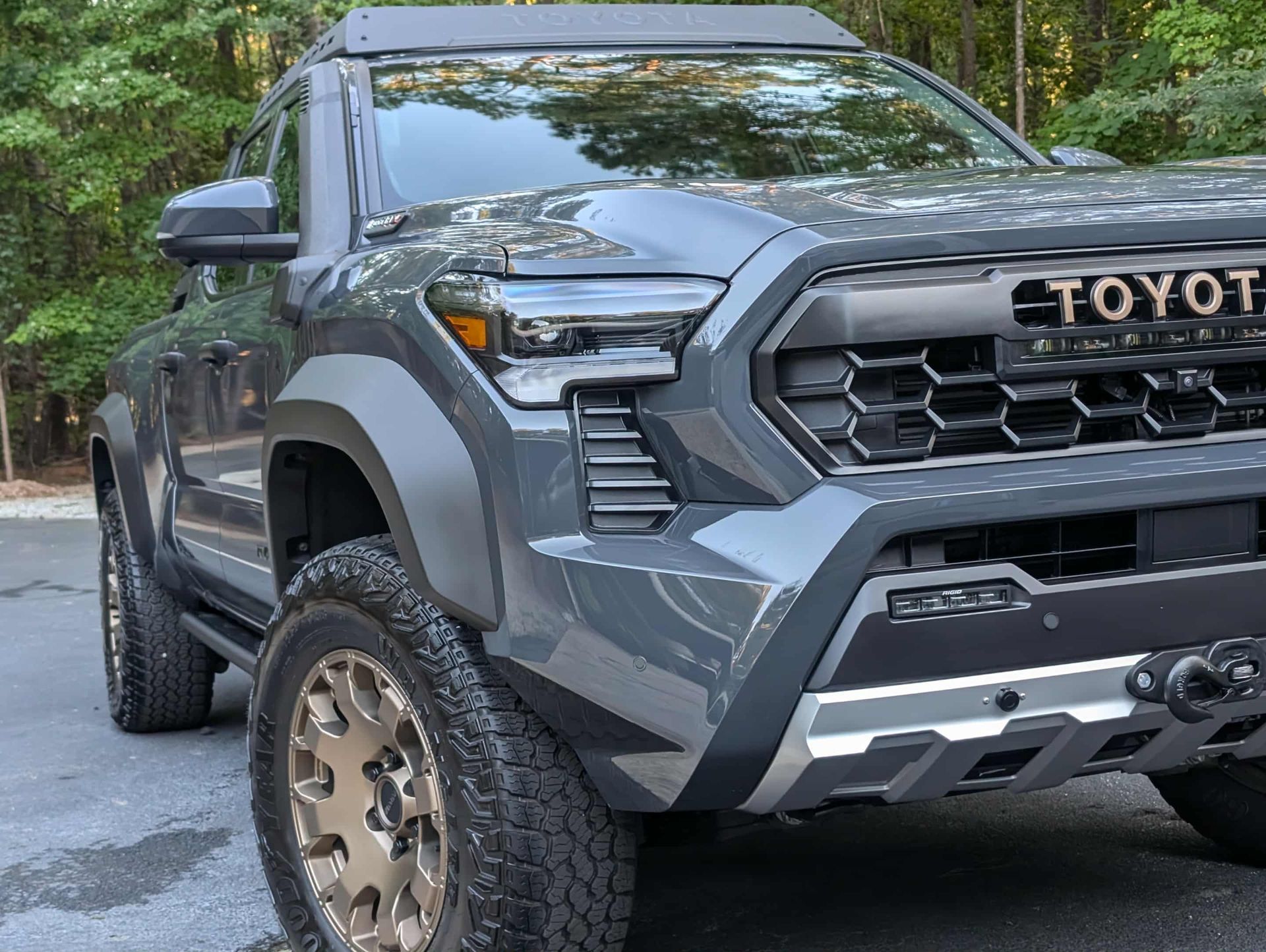 Gray Toyota truck with off-road tires, black accents, and a roof rack, parked outdoors.