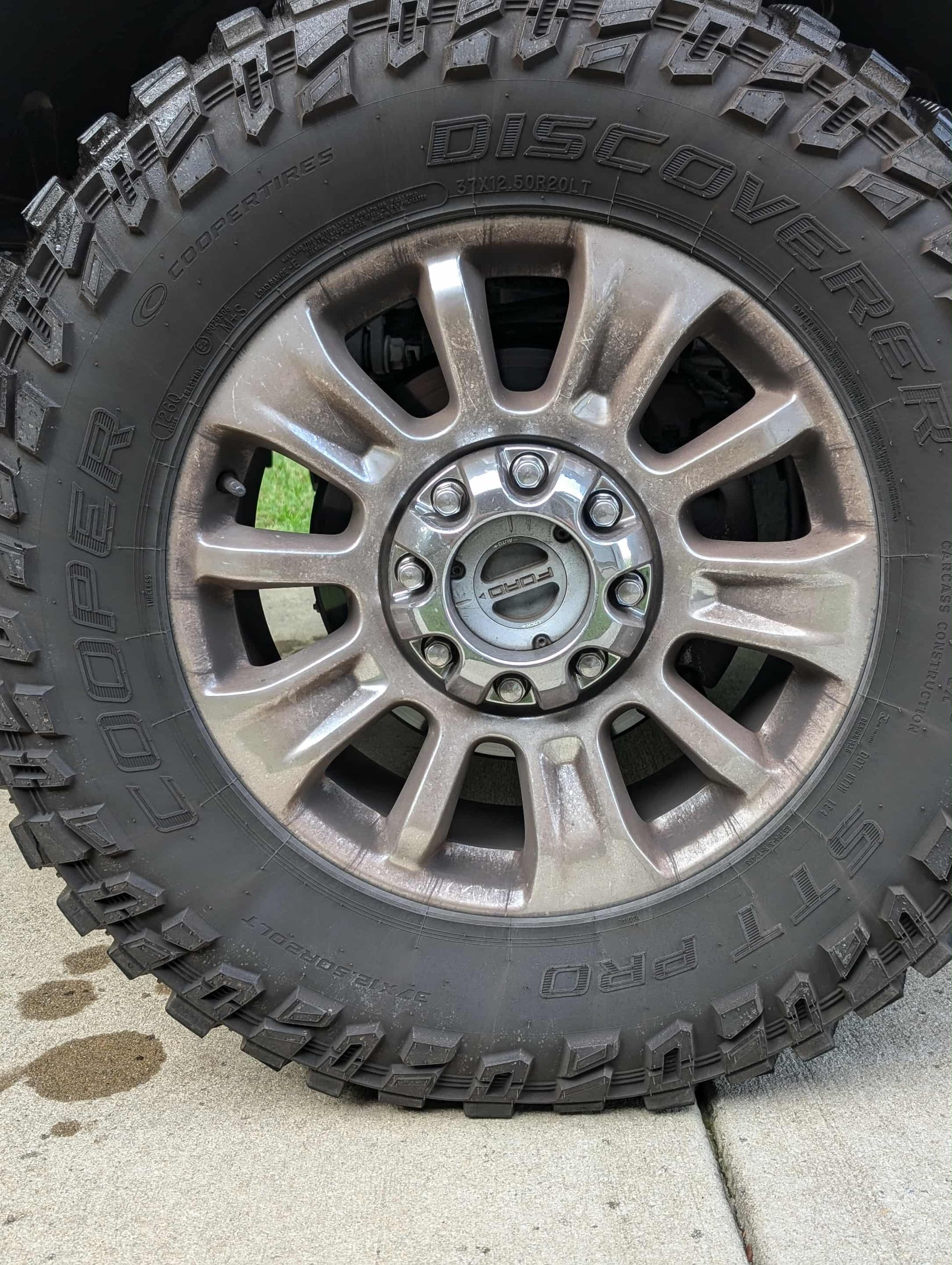 A dirty truck wheel with mud terrain tire on a gray concrete surface.