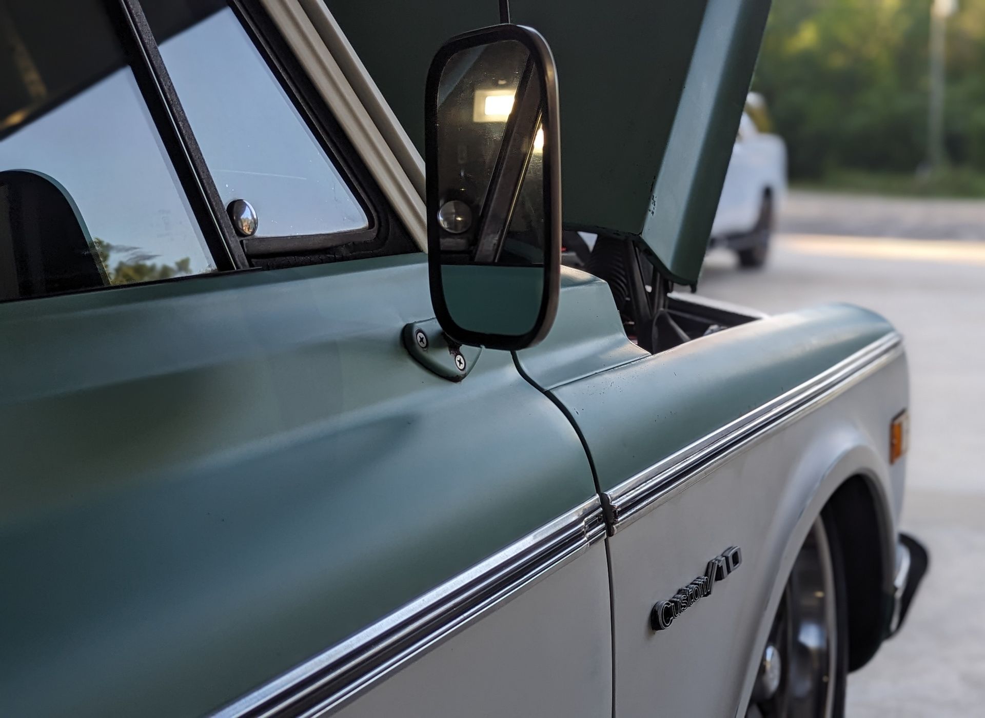 Green and white vintage truck with open hood; side mirror reflects sunlight.