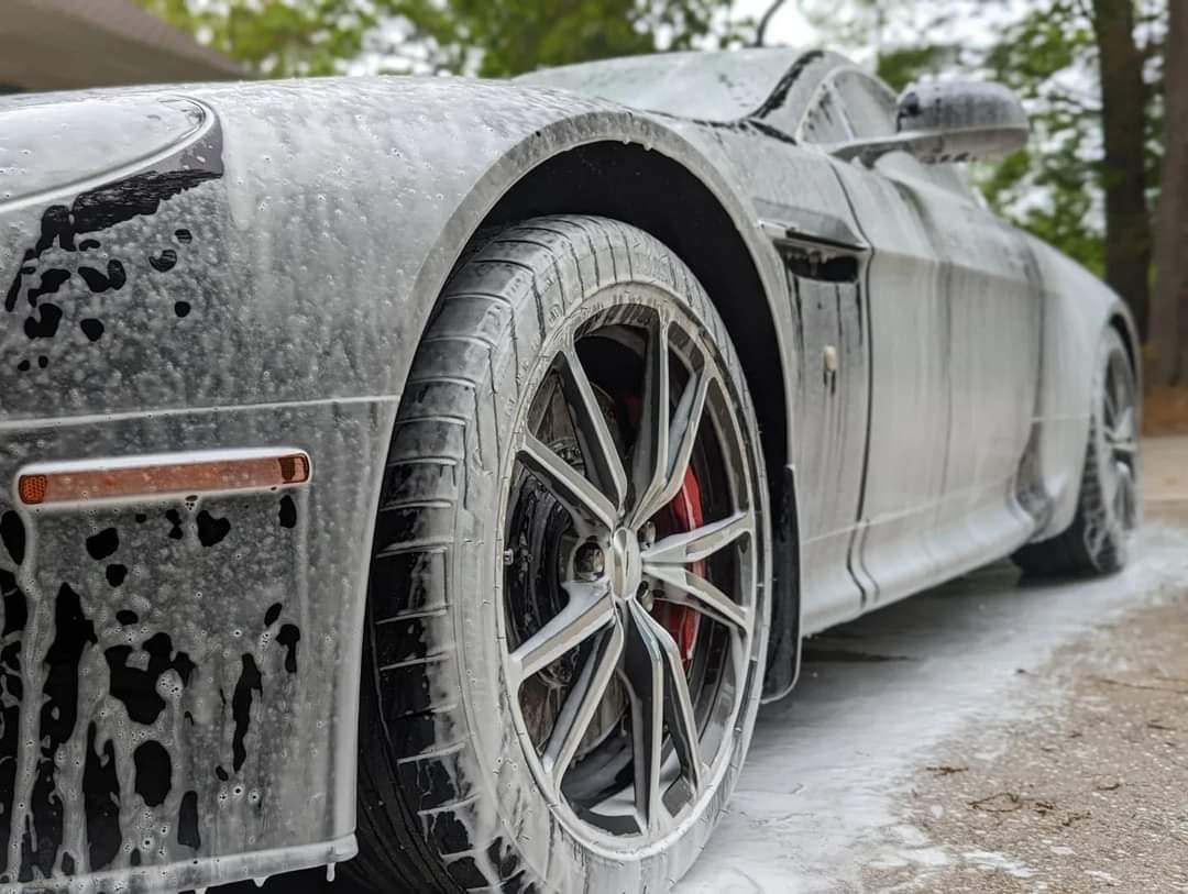 A grey sports car covered in white soap suds during a car wash.