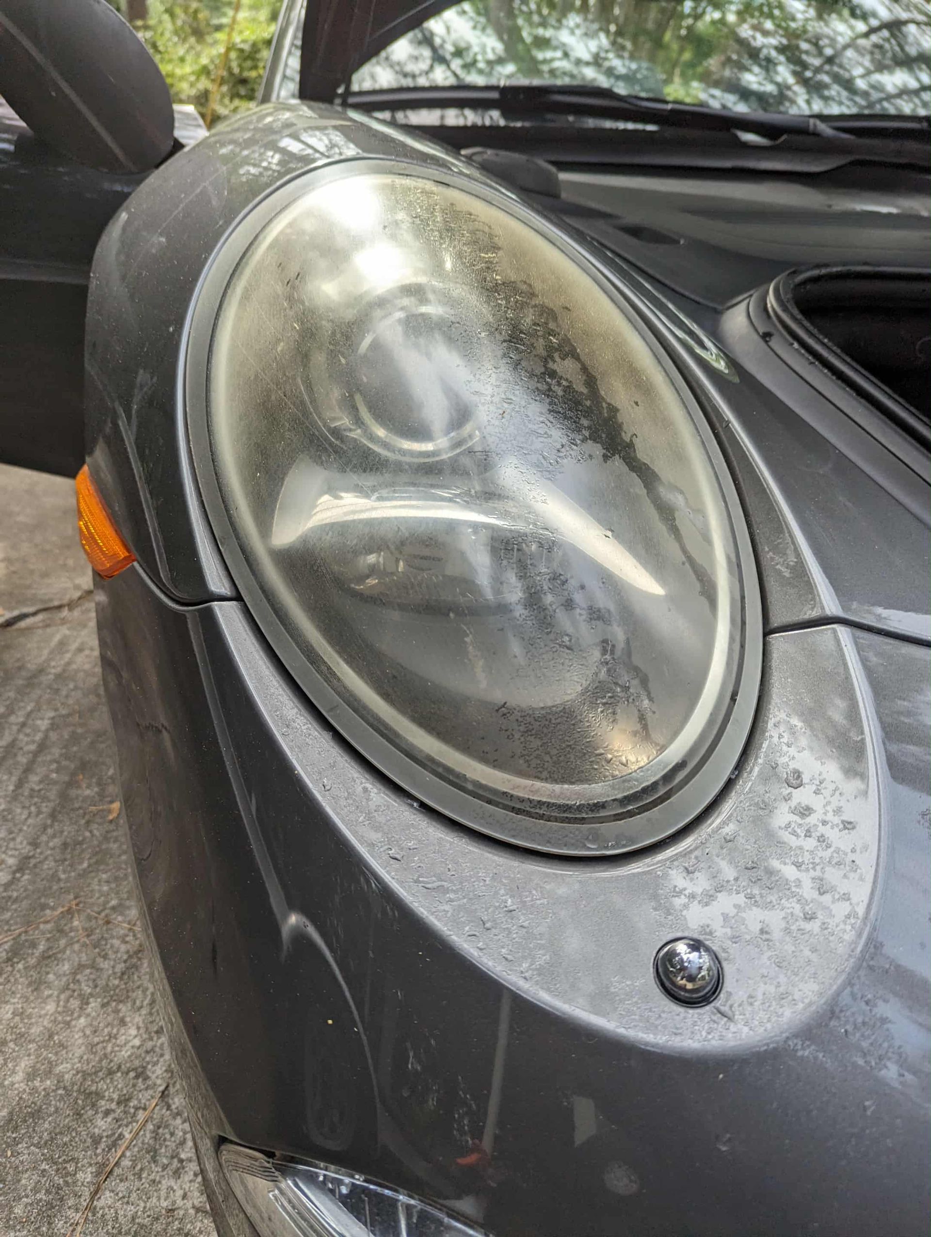 Gray car headlight with condensation and surrounding road grime.