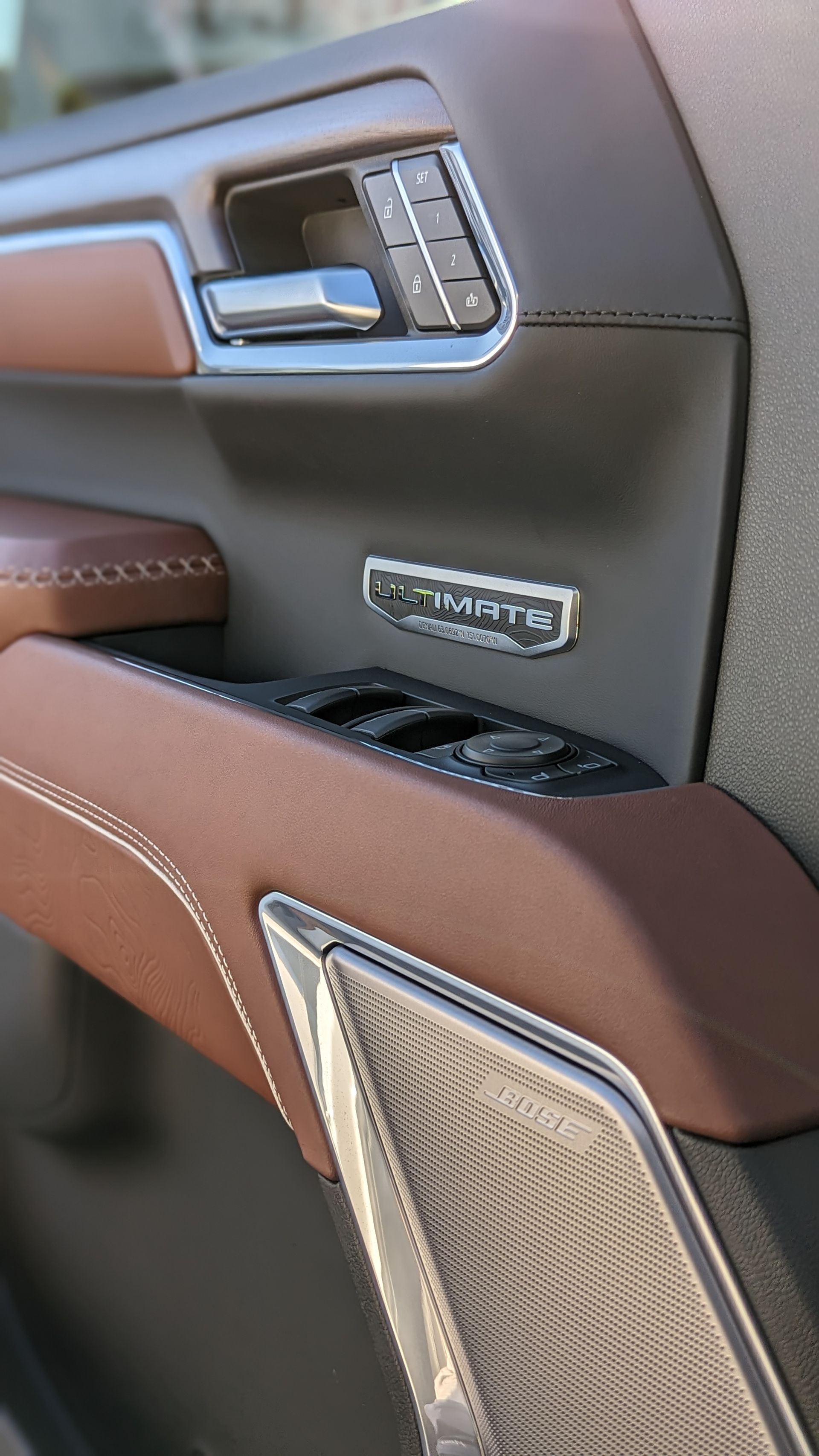 Brown and black car door interior, with stitched leather armrest and silver control buttons.