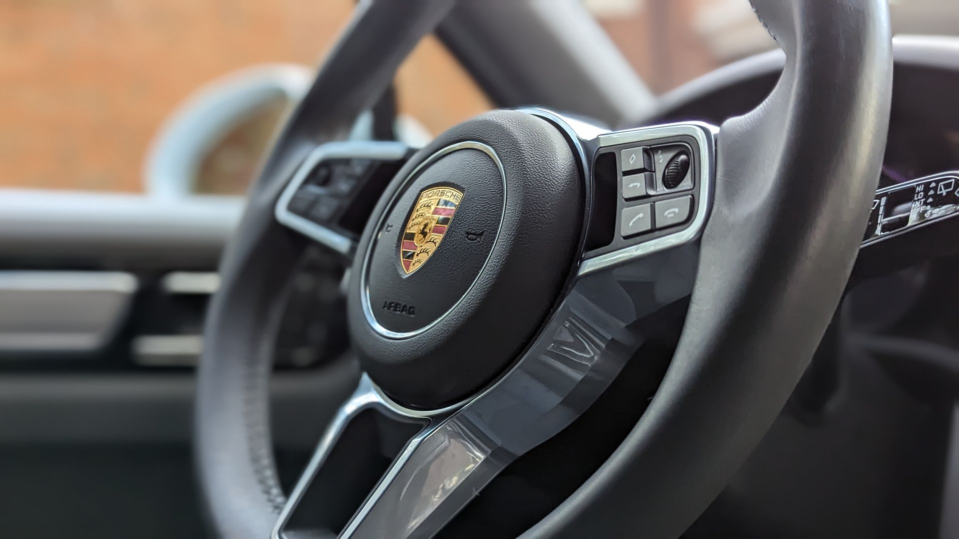 Porsche steering wheel with the brand's emblem in the center, control buttons, and a gray interior.