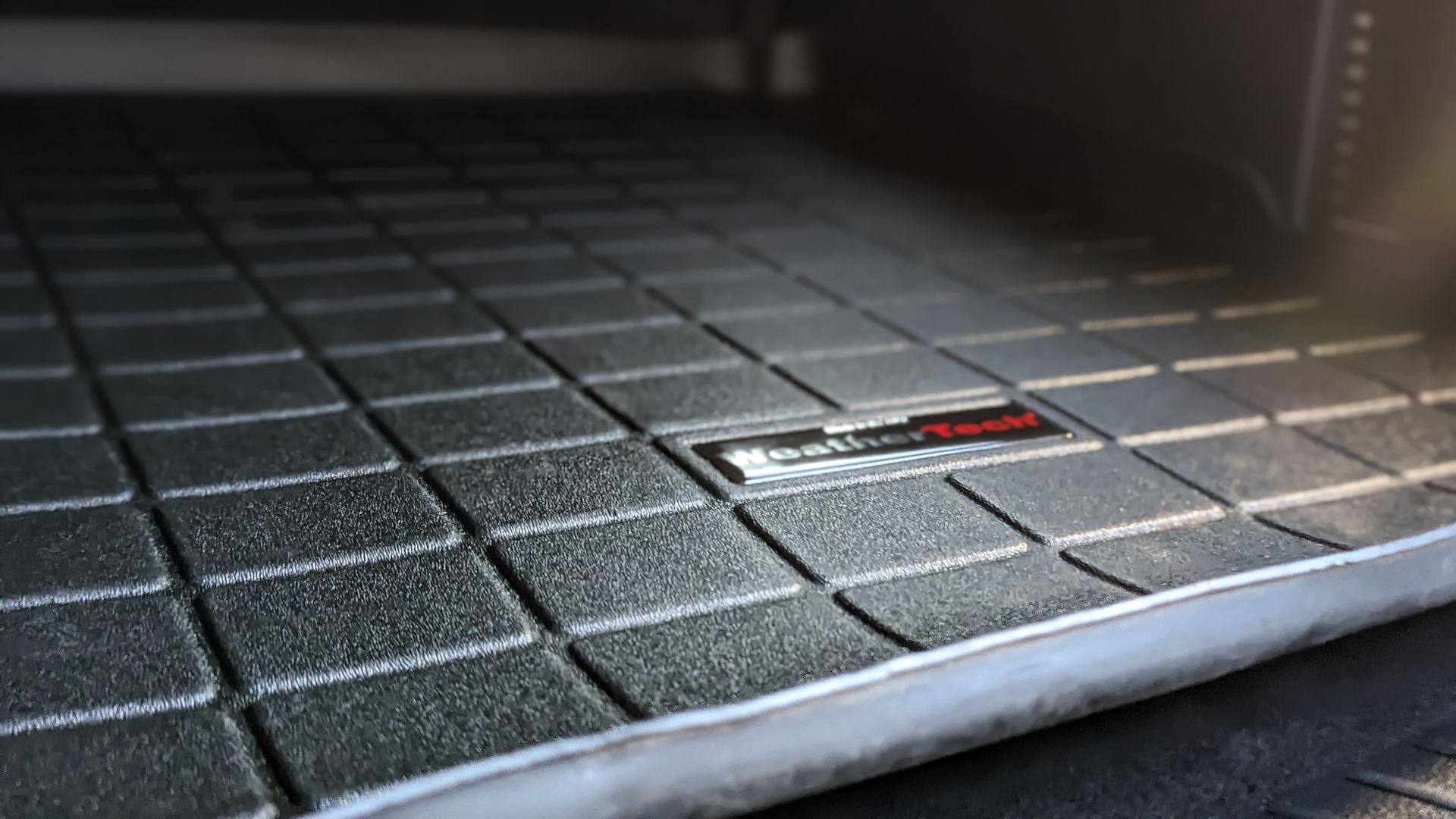 Black rubber floor mat with grid pattern in a vehicle.