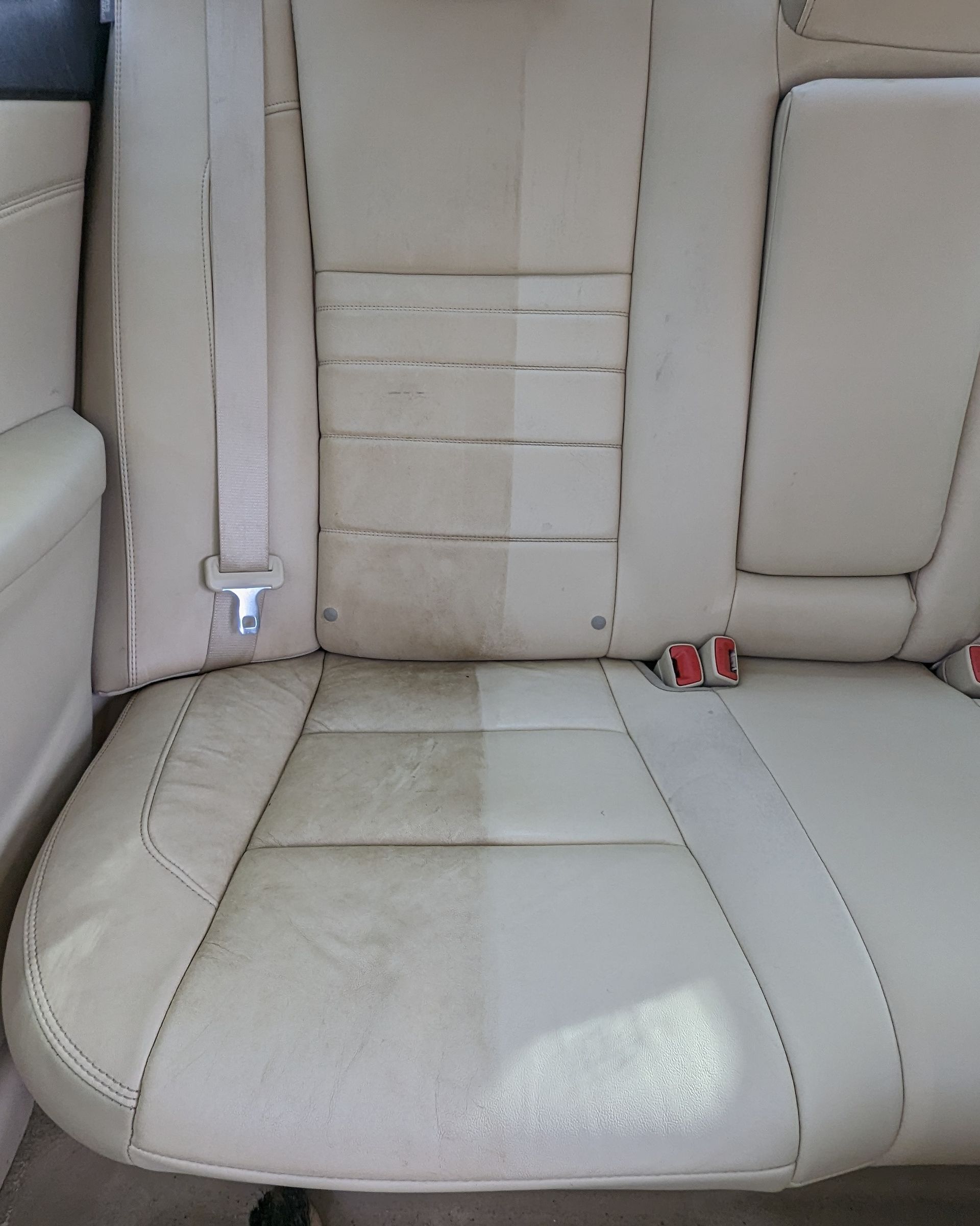 Car's leather back seat, half cleaned, showing stark contrast. Beige seat, dirt on the uncleaned half.