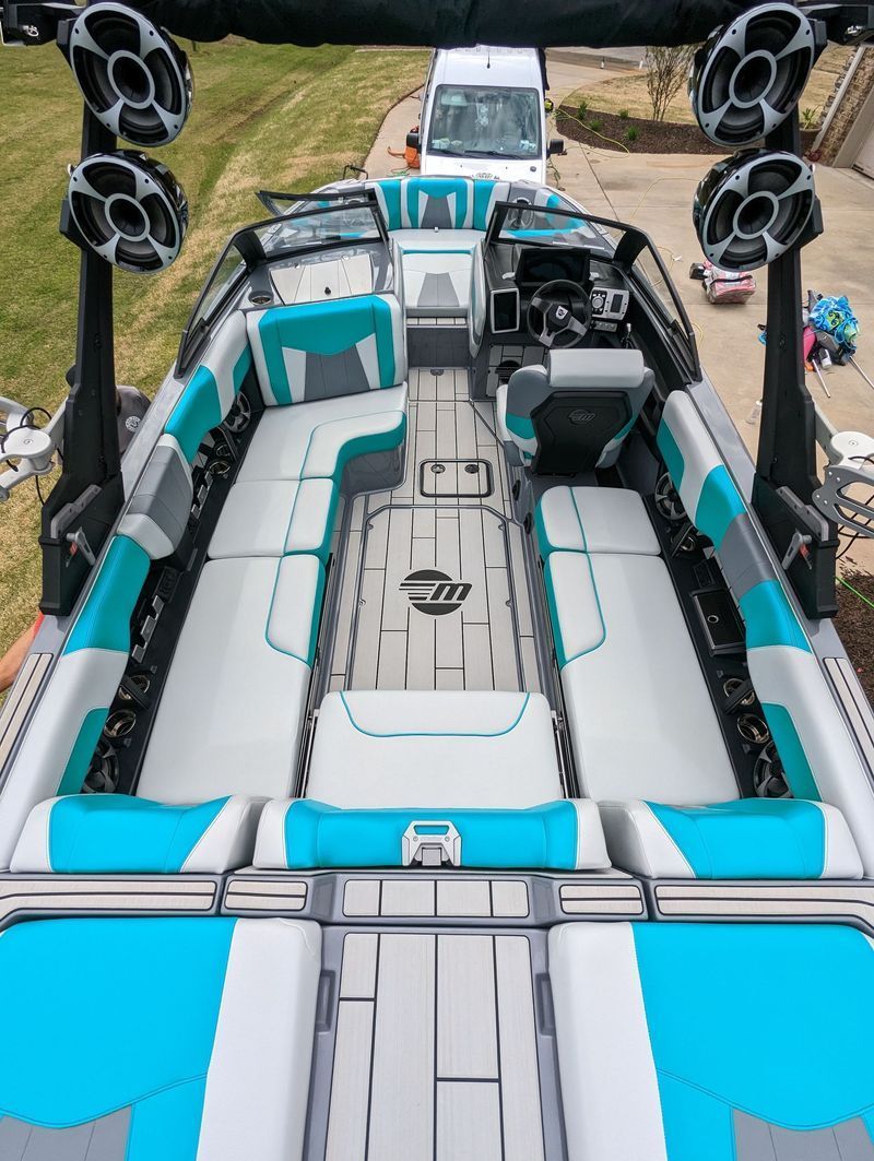 A high-angle view of a motorboat with teal and gray upholstery, black speakers, and a white van in the background.