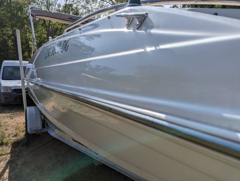 White motorboat on a trailer, parked outdoors. Shiny hull, curved lines, stainless steel rails.