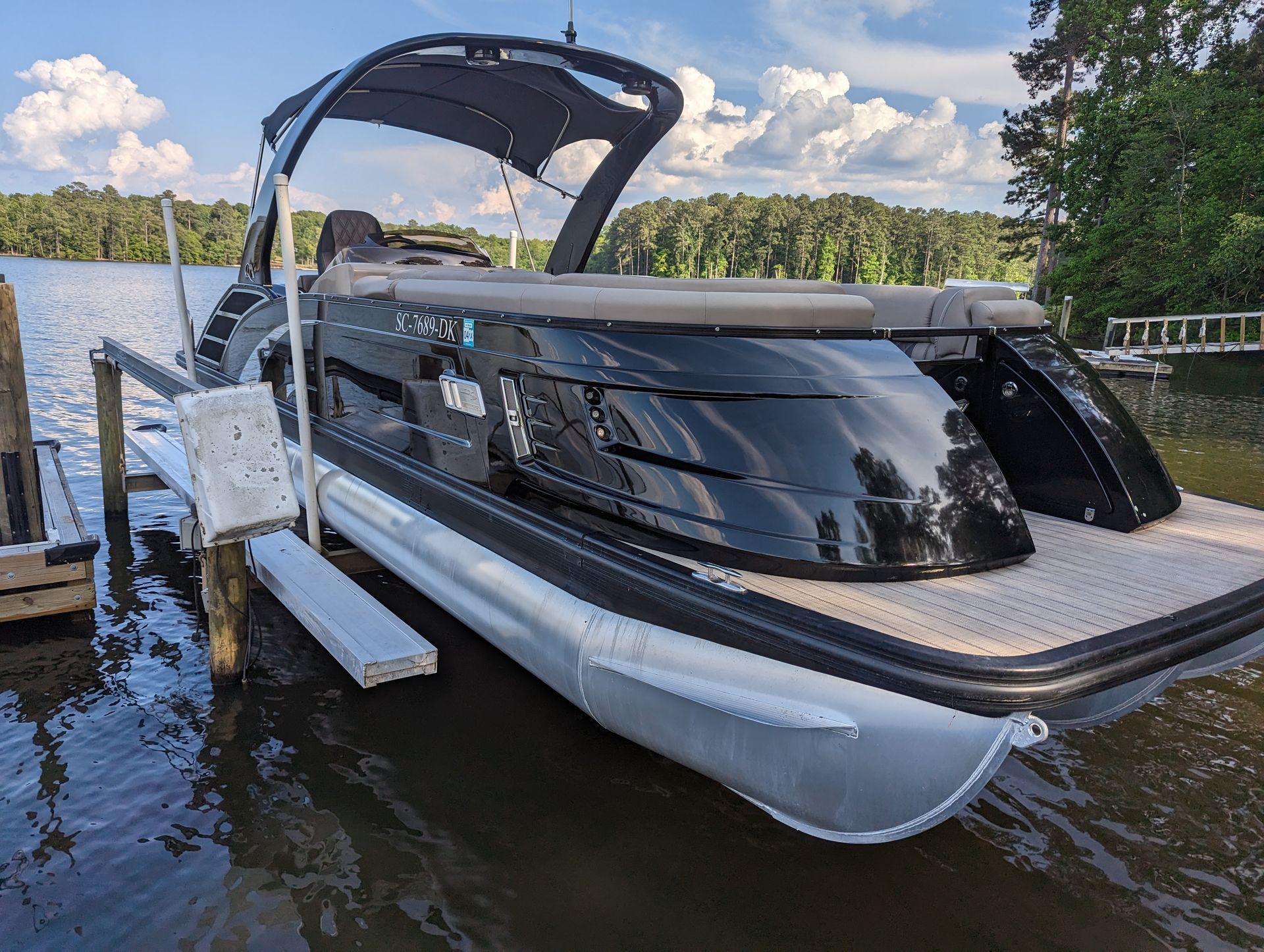 Black and silver pontoon boat docked on a lake with a dark canopy.