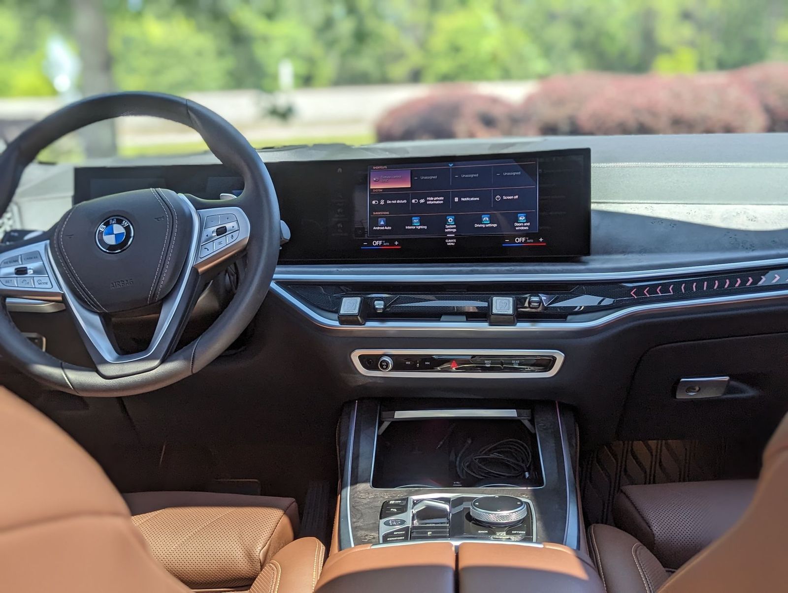 BMW car interior with large screen display, steering wheel, and tan leather seats.