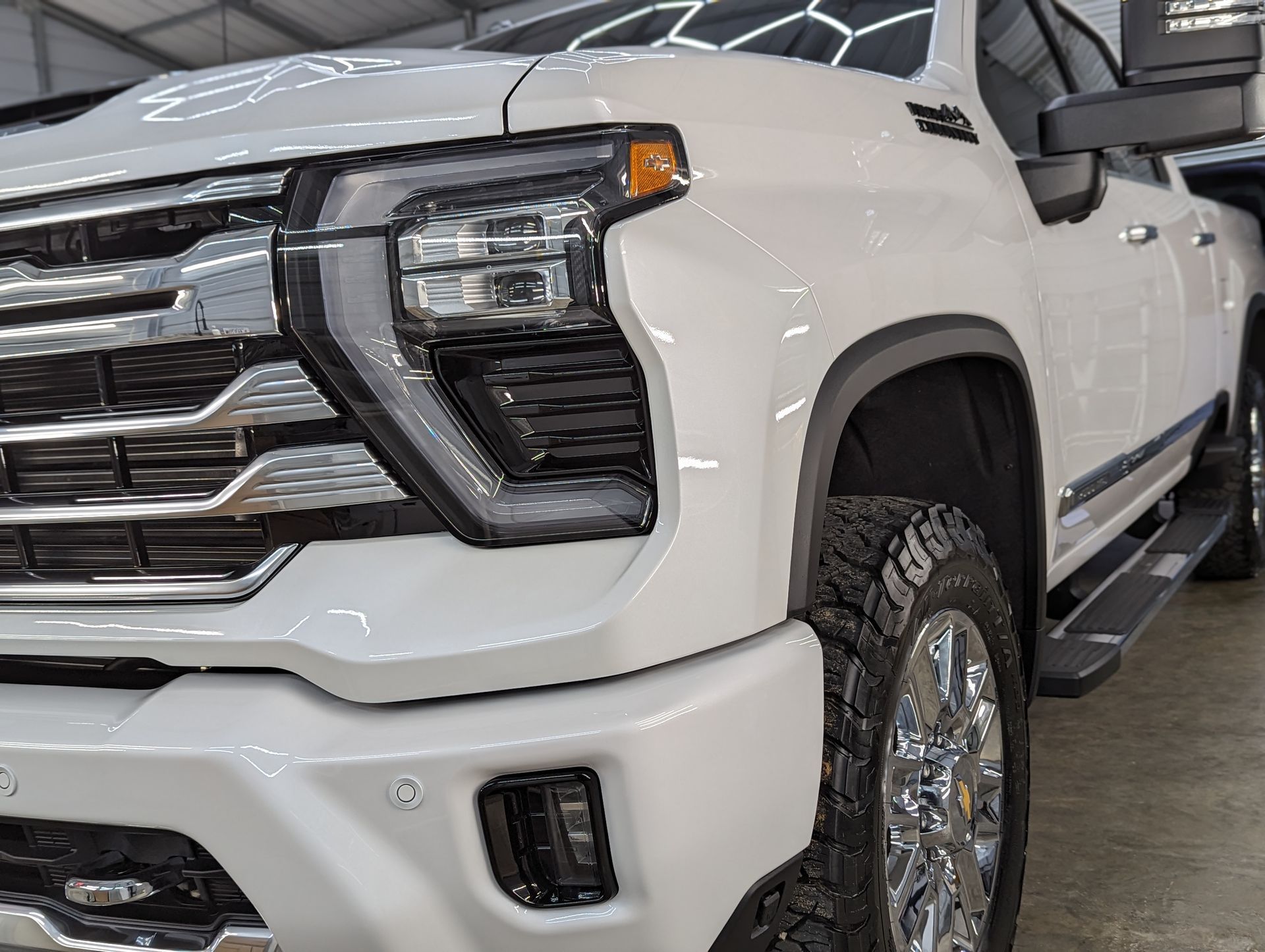 White Chevrolet truck, front quarter view, showing the grill, headlight, tire, and chrome details.