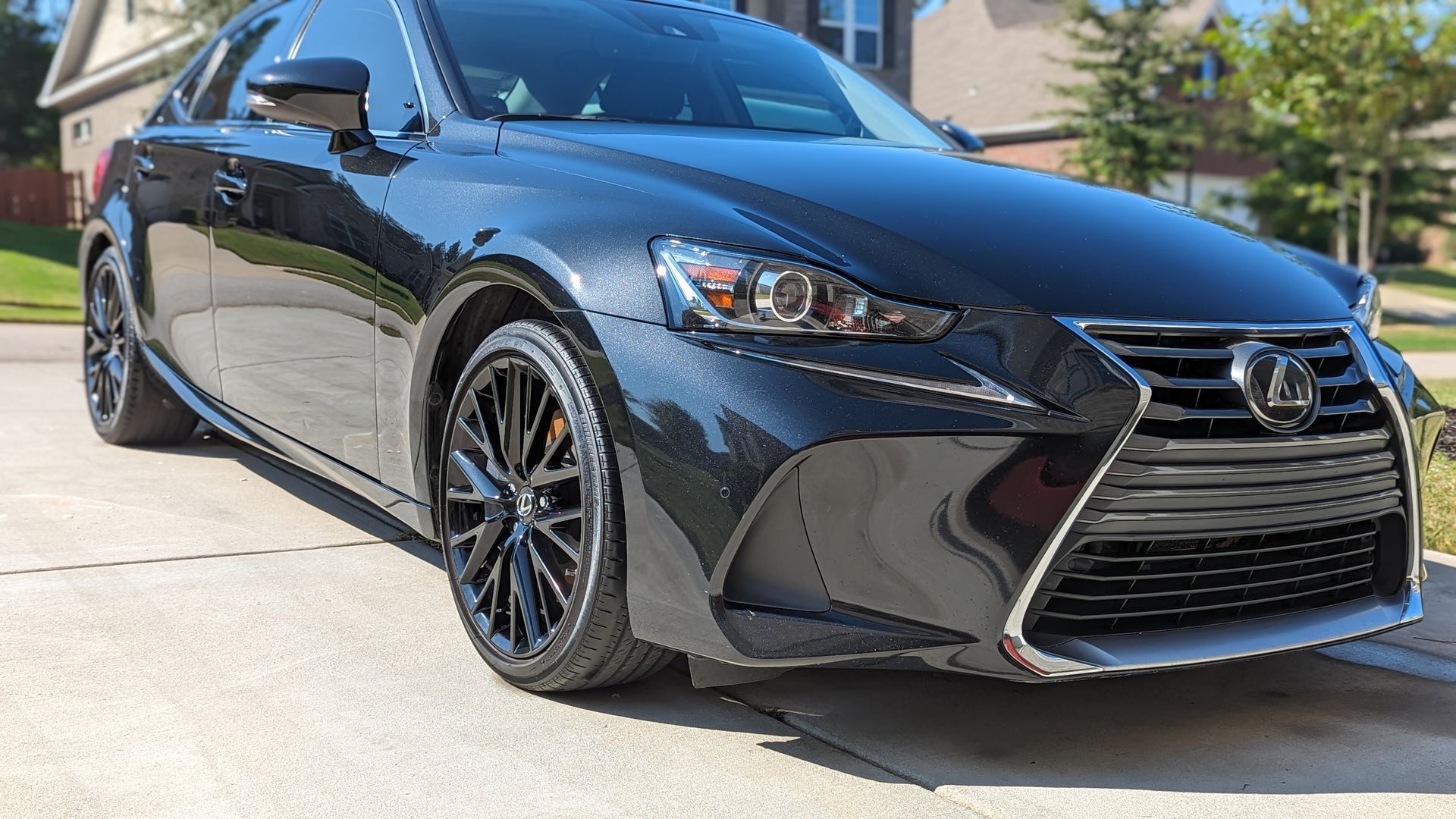 Black Lexus sedan parked on a driveway, shiny paint, black rims, front view.