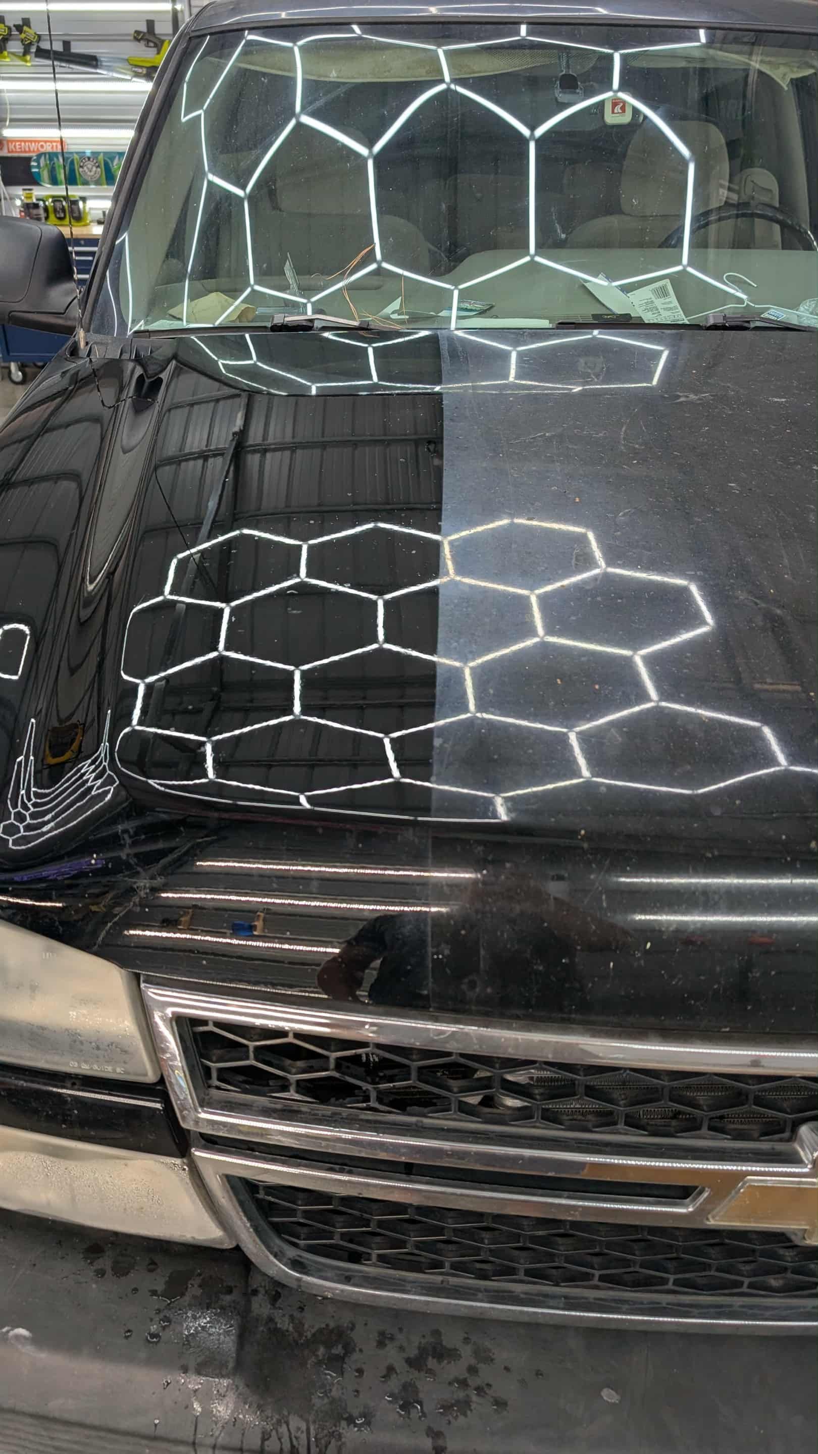 Black car hood, half-polished showing a stark contrast. The reflection of honeycomb-shaped lights is visible.