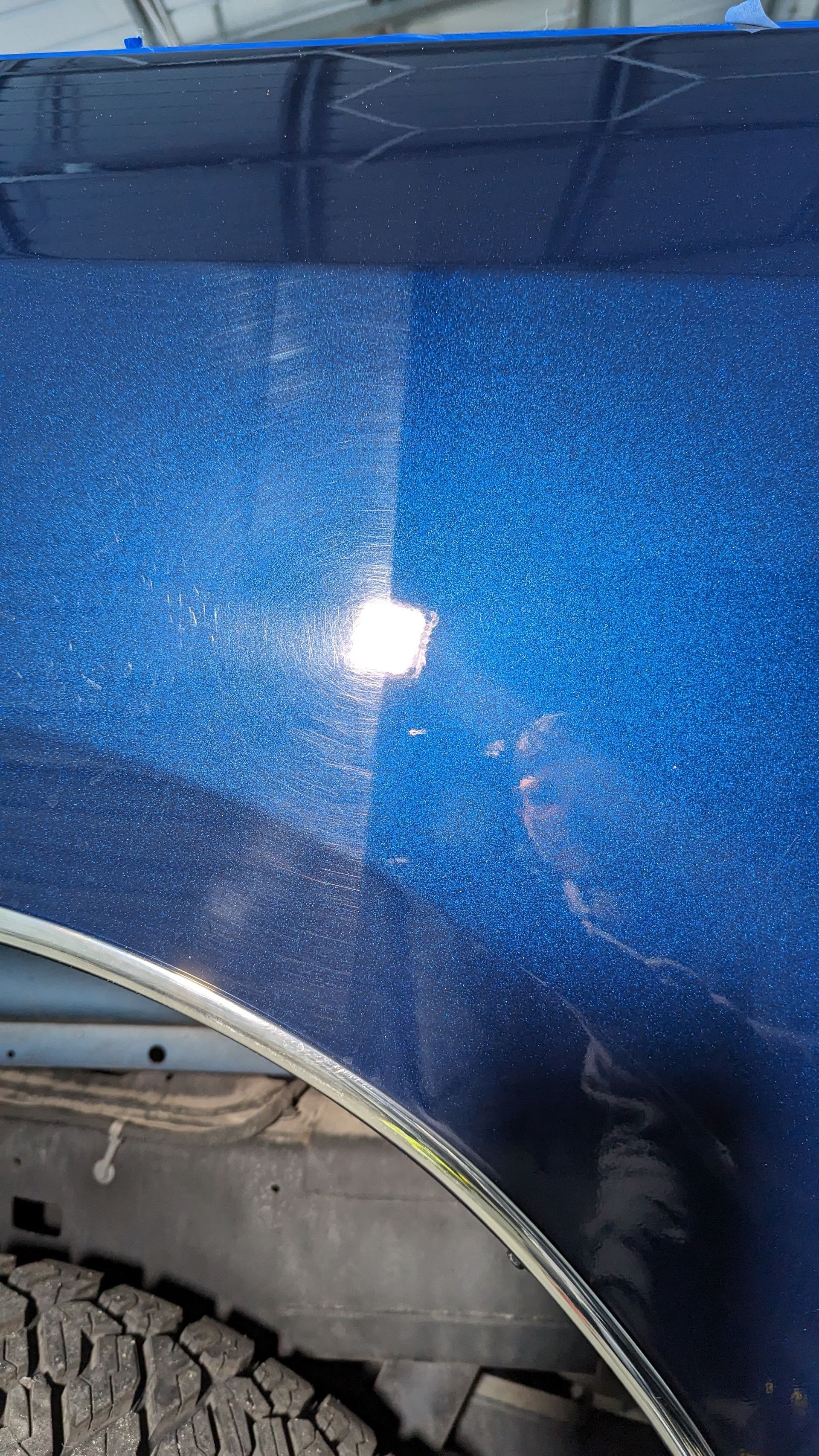 A blue car panel with noticeable scratches and glitter. A polished section contrasts the unpolished area.