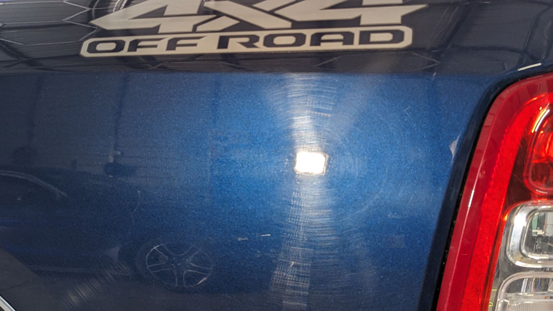 Blue truck bed with 4x4 Off Road decal; visible scratches and a red taillight.