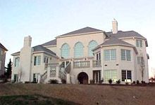 A large white house with a gray roof is sitting on top of a dirt hill.