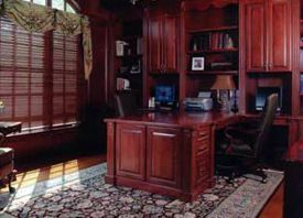 A home office with a desk , chairs , shelves and a rug.