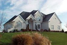 A large white house with a black roof is sitting on top of a lush green hill.