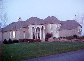 A large brick house with a gray roof is sitting on top of a lush green lawn.