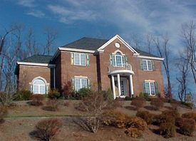 A large brick house is sitting on top of a hill surrounded by trees.