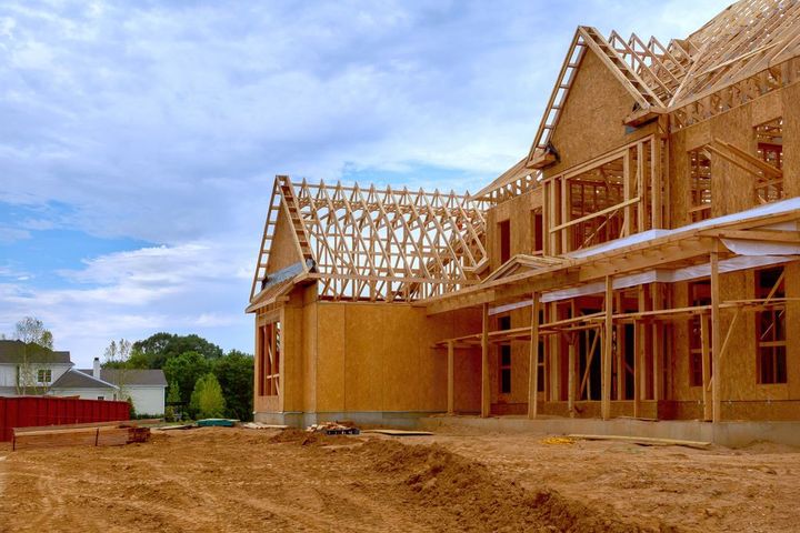 A large wooden house is being built in a dirt field.