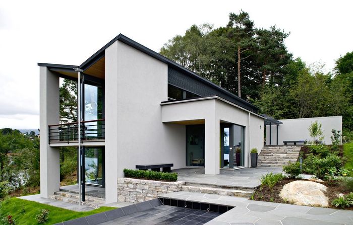 A white house with a black roof is sitting on top of a hill surrounded by trees.