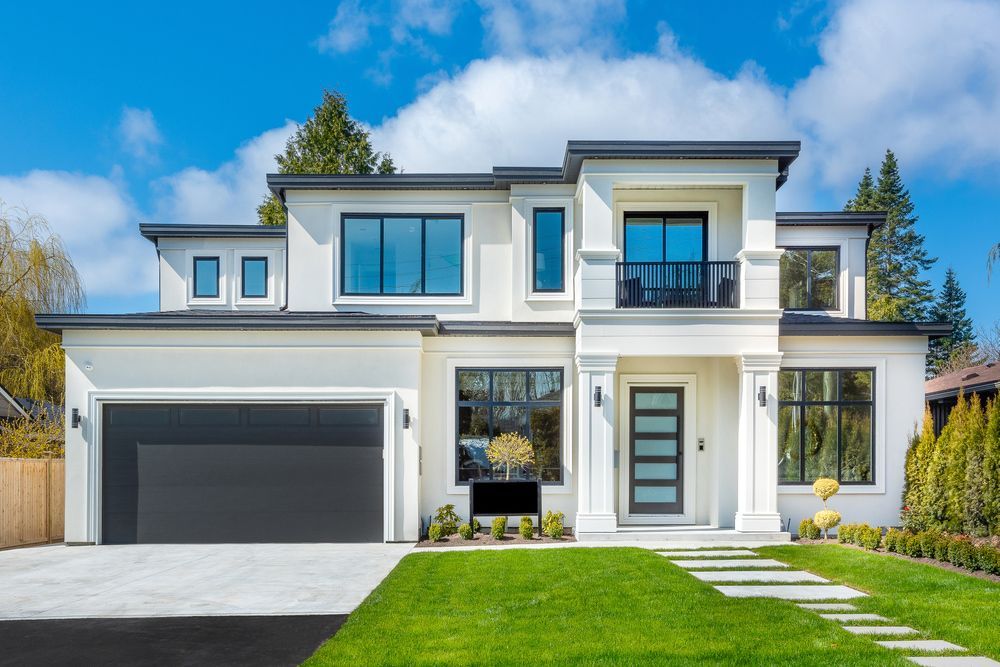 A large white house with a black garage door and a lush green lawn.