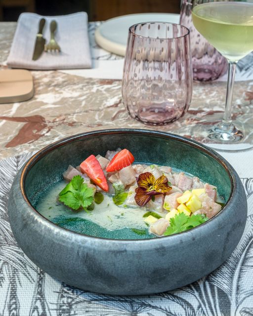 Un piatto bianco di cremoso risotto guarnito con tre piccole vongole e diverse fette di pesce affumicato, il tutto condito con un filo d'olio.