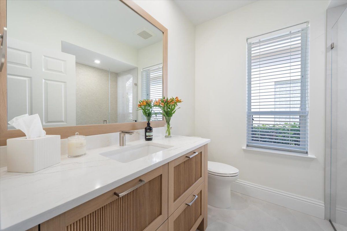 A bathroom with a sink, toilet, mirror and window.