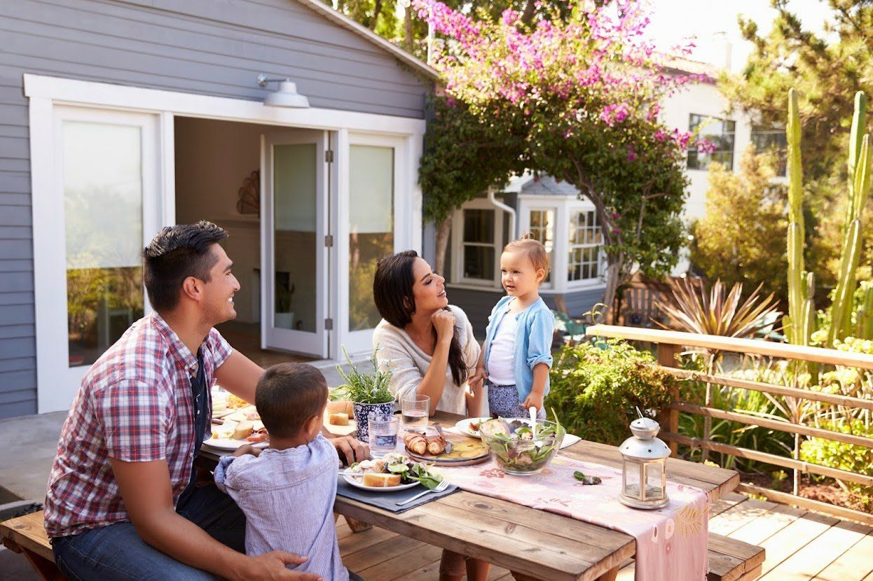 A family is sitting at a picnic table outside their house.