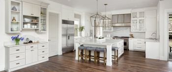 A kitchen with white cabinets, hardwood floors, stools and a large island.