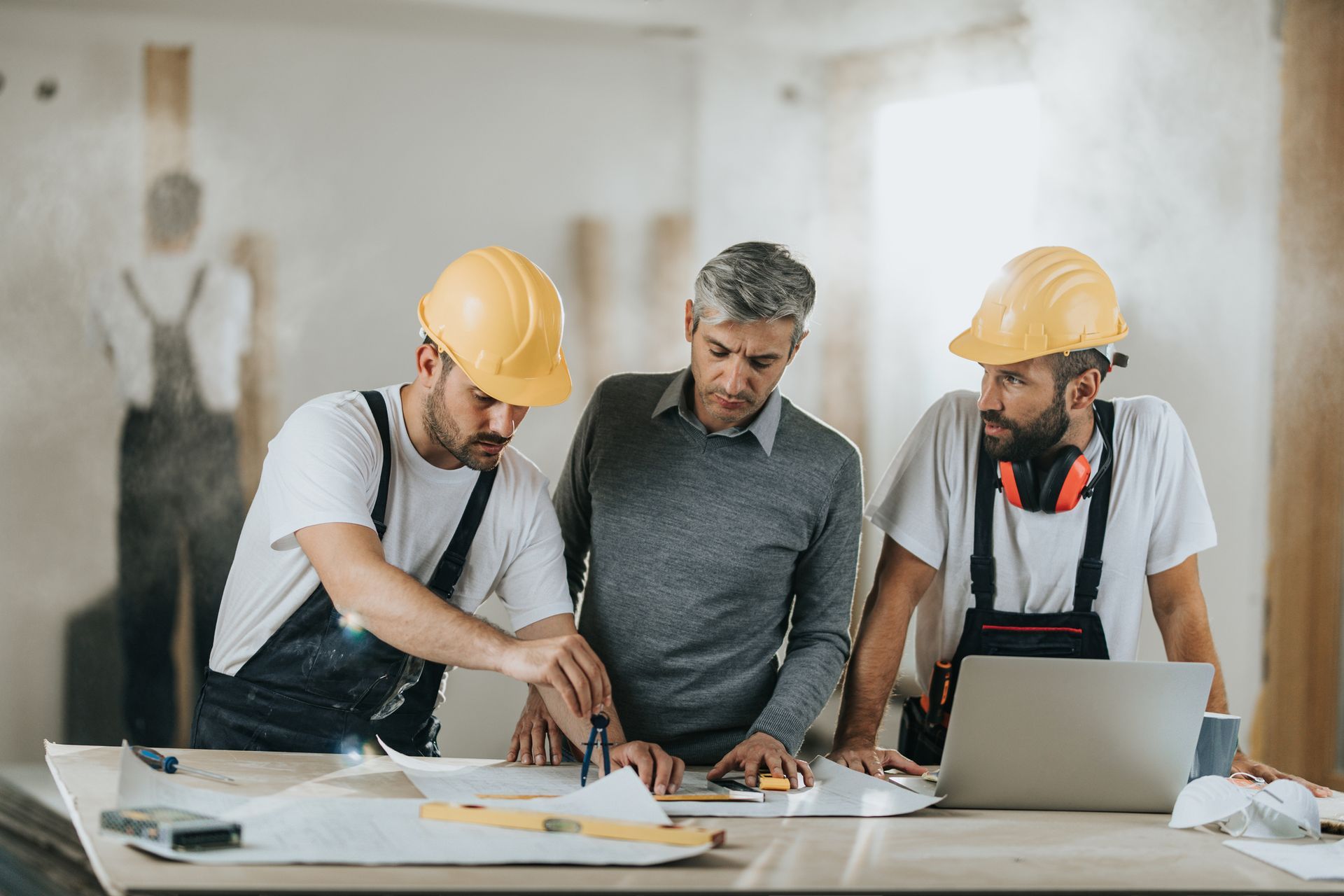 Renovation contractors are examining blueprints with a client at the construction site.