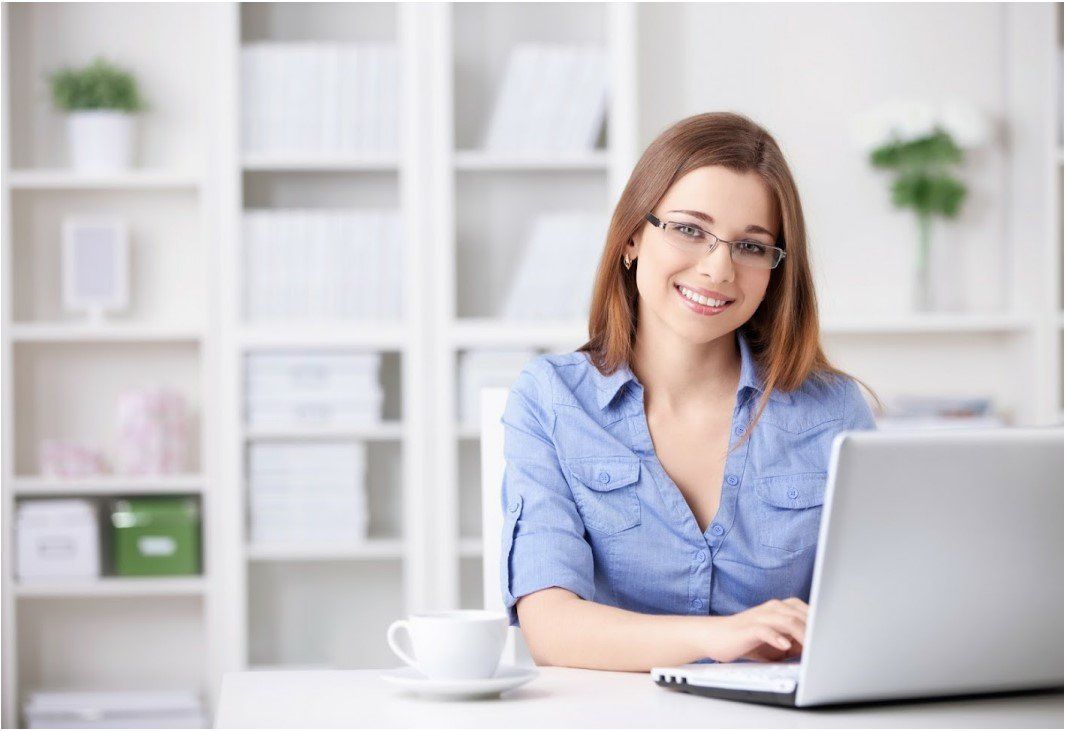 A woman is sitting at a desk with a laptop and a cup of coffee.