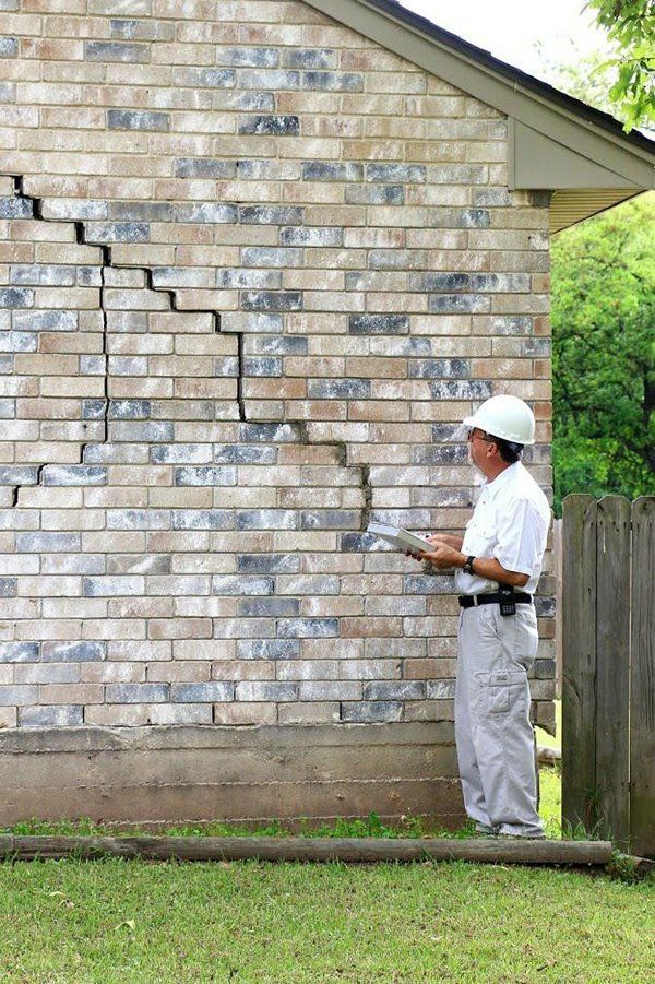 A man is standing in front of a cracked brick wall.