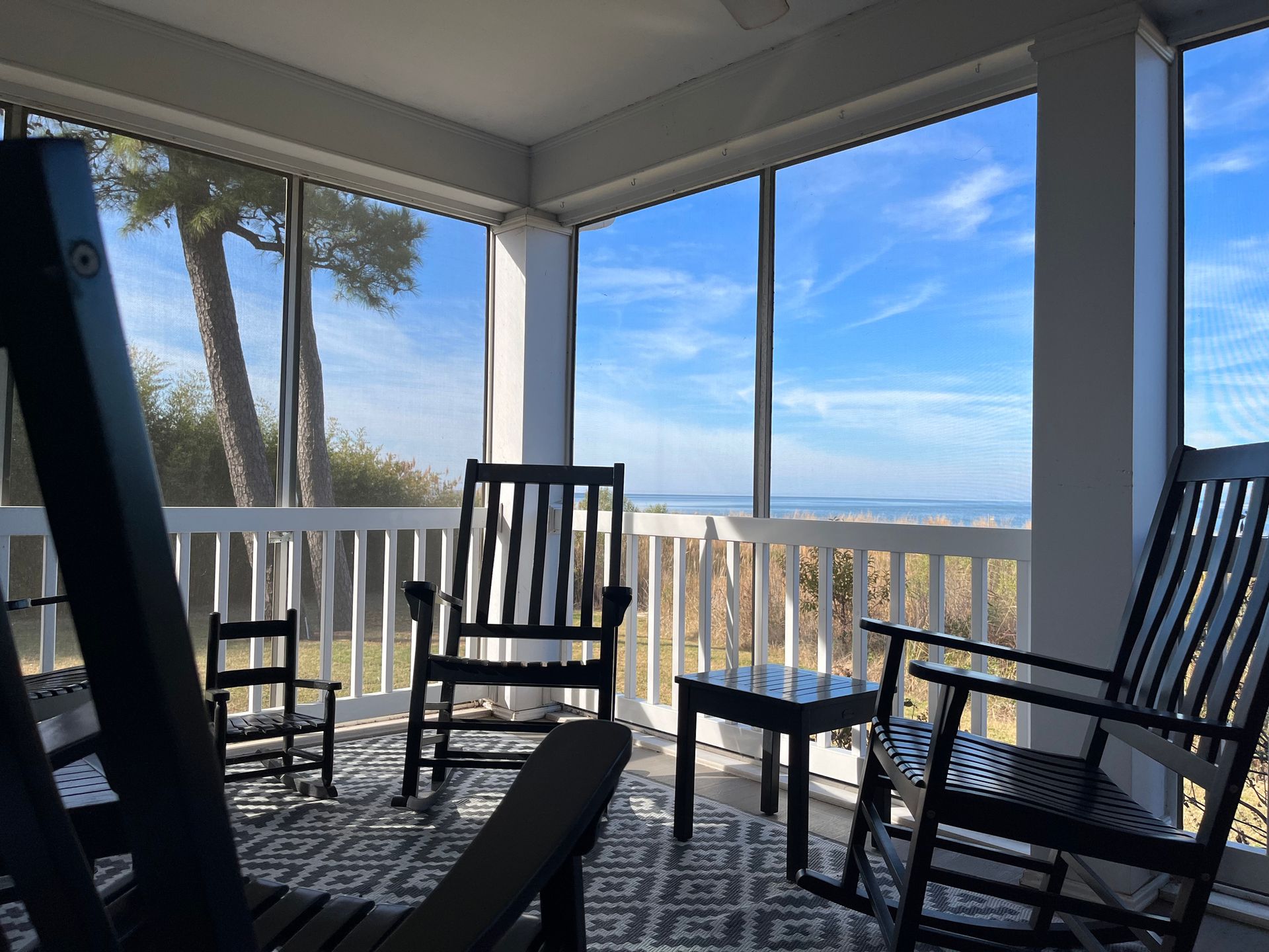 Veranda protetta da zanzariere con sedie a dondolo, vista sull'oceano e cielo azzurro brillante.