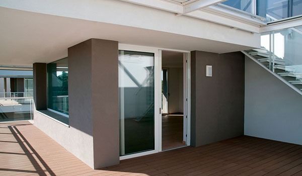 Vista esterna di un edificio moderno con pareti marroni, porta bianca aperta e scala.